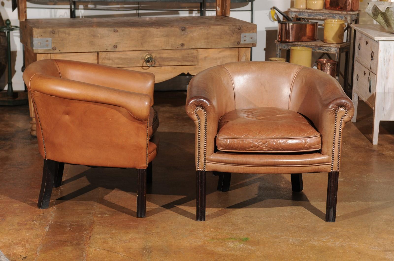 One pair of Italian vintage caramel leather club chairs from the mid-20th century, with cushion, dark brown legs and brass nail-head trim.  Born in Italy during the mid-century period, this pair of leather club chairs presents a horse back with