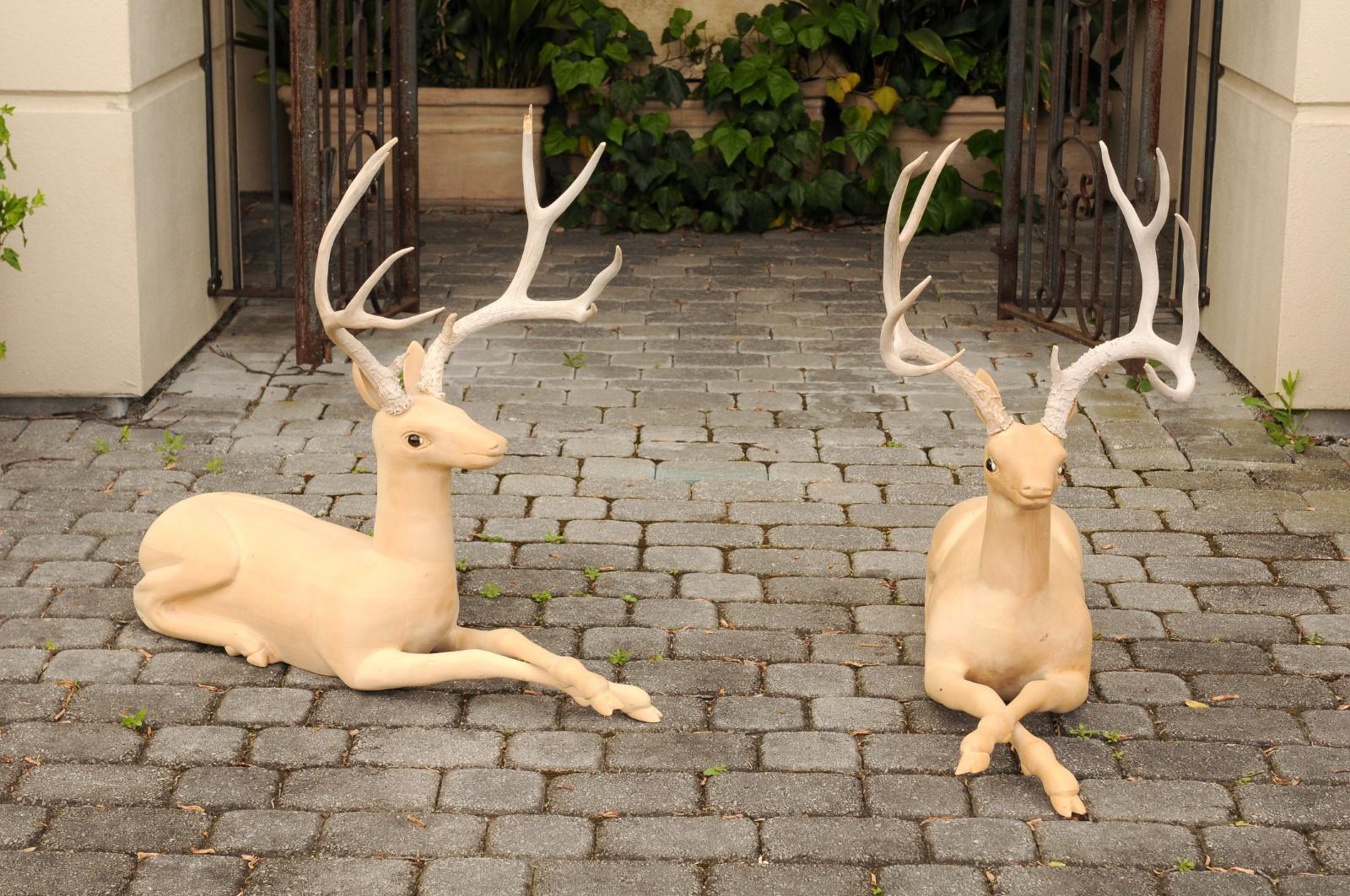 A pair of Italian wooden carved stag sculptures from the mid-20th century with large antlers. Born in Italy during the mid-century period, this charming pair of wooden sculptures depicts two stags carved in a minimalist style and topped with large
