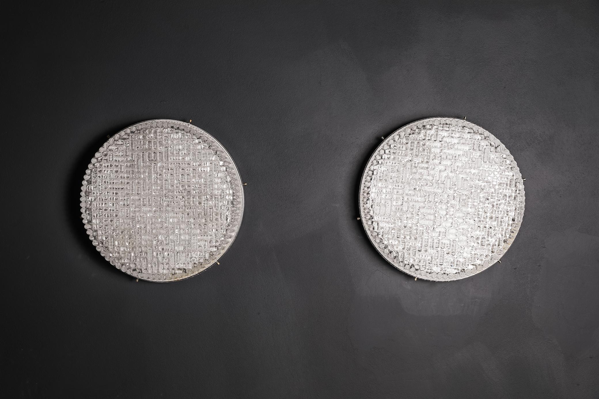 Impressive pair of 1970 wall lights made from thick textured glass which give a beautiful light and effect when lit. The glass attaches to a metal plate with brass pins. Measures: Diameter 50 cm.