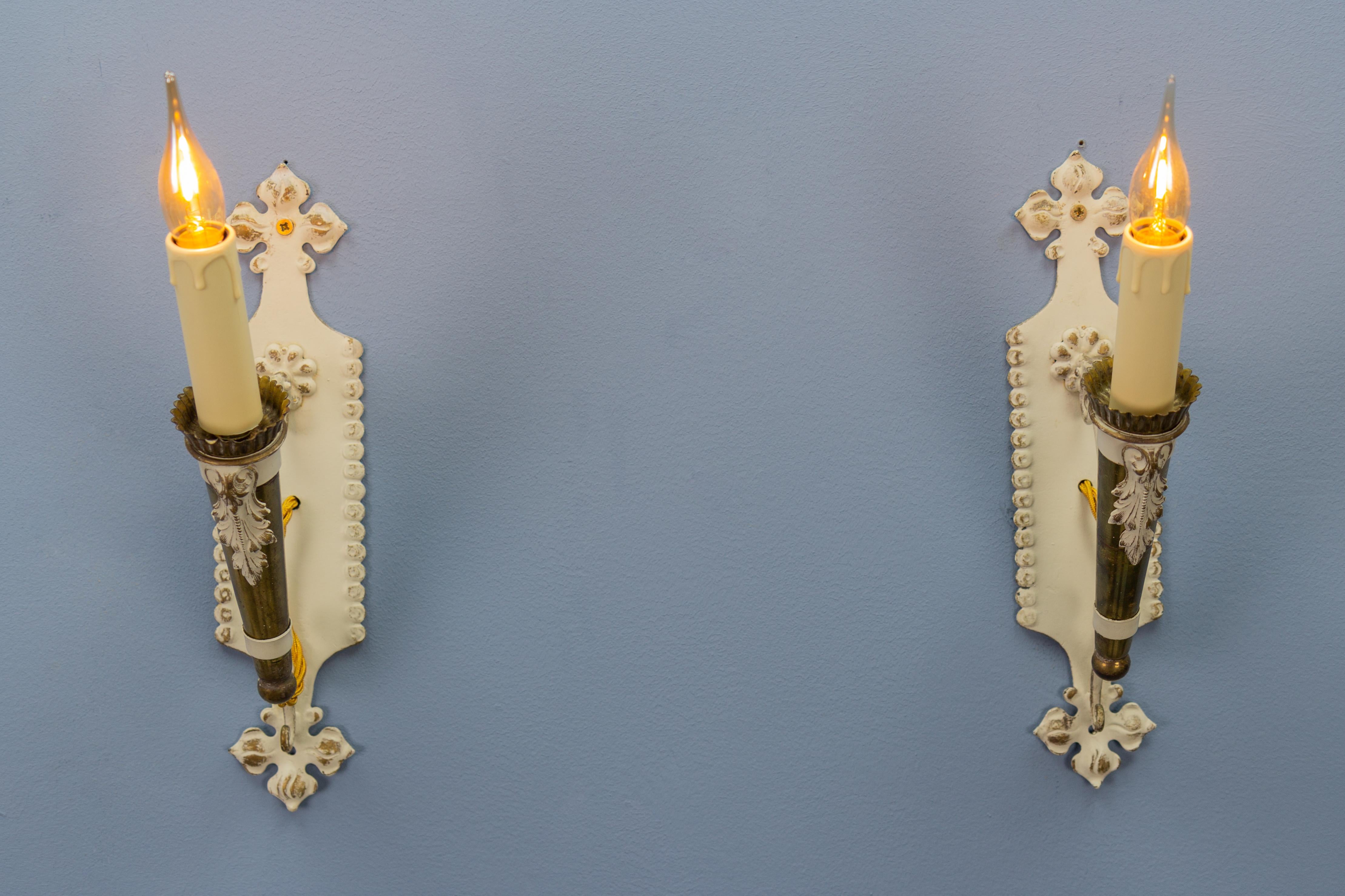 Pair of Italian vintage white and golden metal torch-shaped wall sconces from ca. 1950s.
An adorable pair of Italian single-arm torch-shaped metal wall sconces, beautifully painted in white with golden accents and ornate backplates. Each sconce has