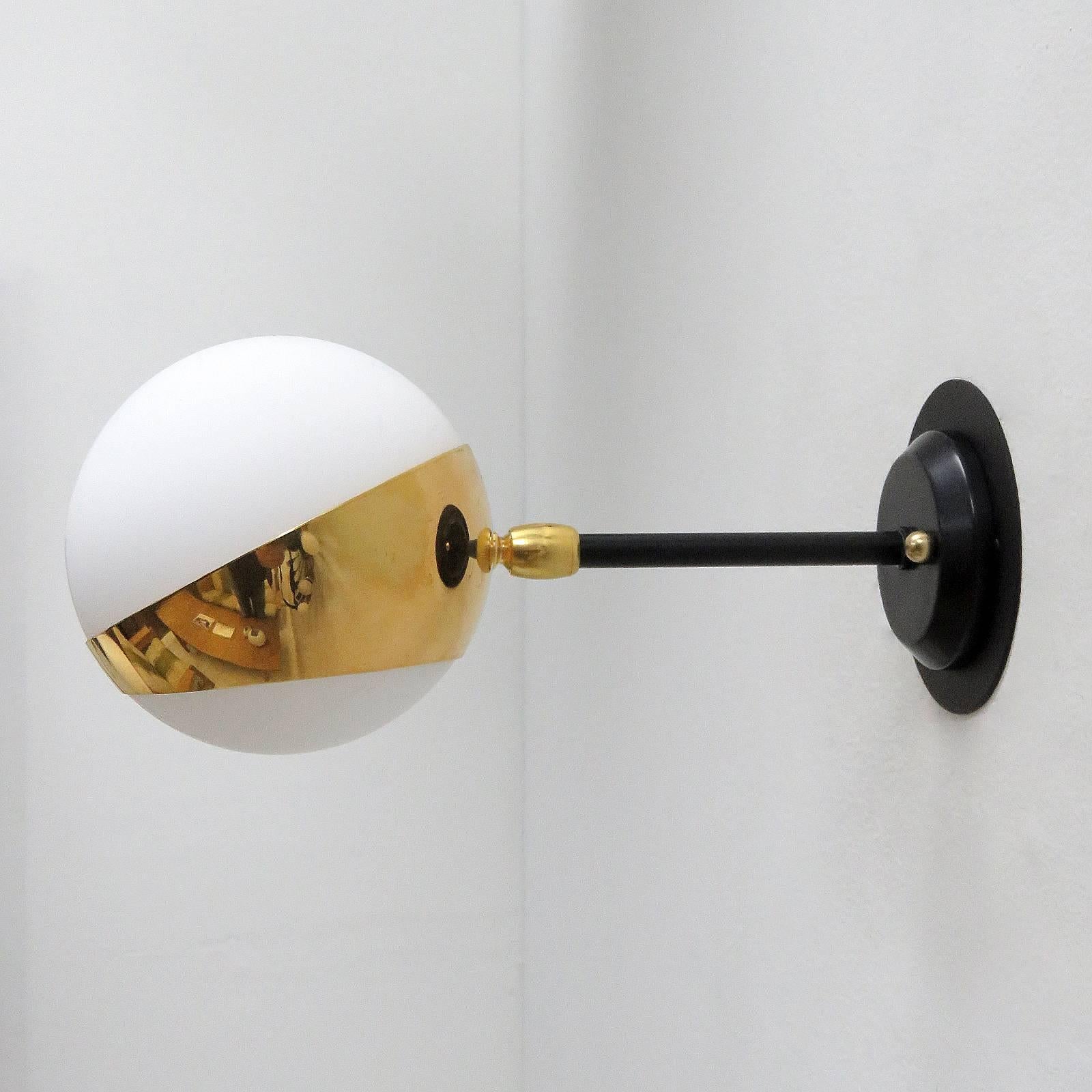 Wonderful pair of Italian wall lights manufactured by Stilnovo, 1950s, with an opaline glass sphere in a partially spherical brass holder on a swivel jointed black enameled arm.