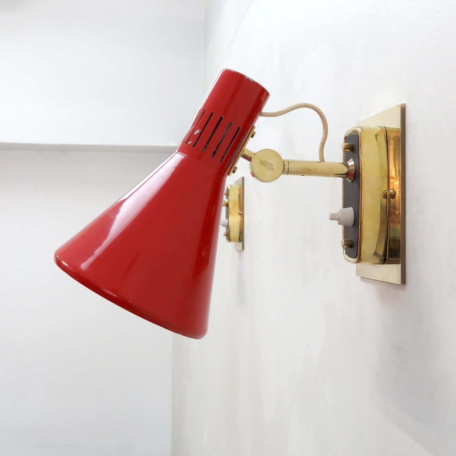Wonderful pair of articulate Italian wall lights Model 2085 by Bruno Gatta, manufactured by Stilnovo, 1950s, with red enameled, perforated shades on swivel brass arms, individual on/off switch on each backplate, custom solid brass backplate, marked,