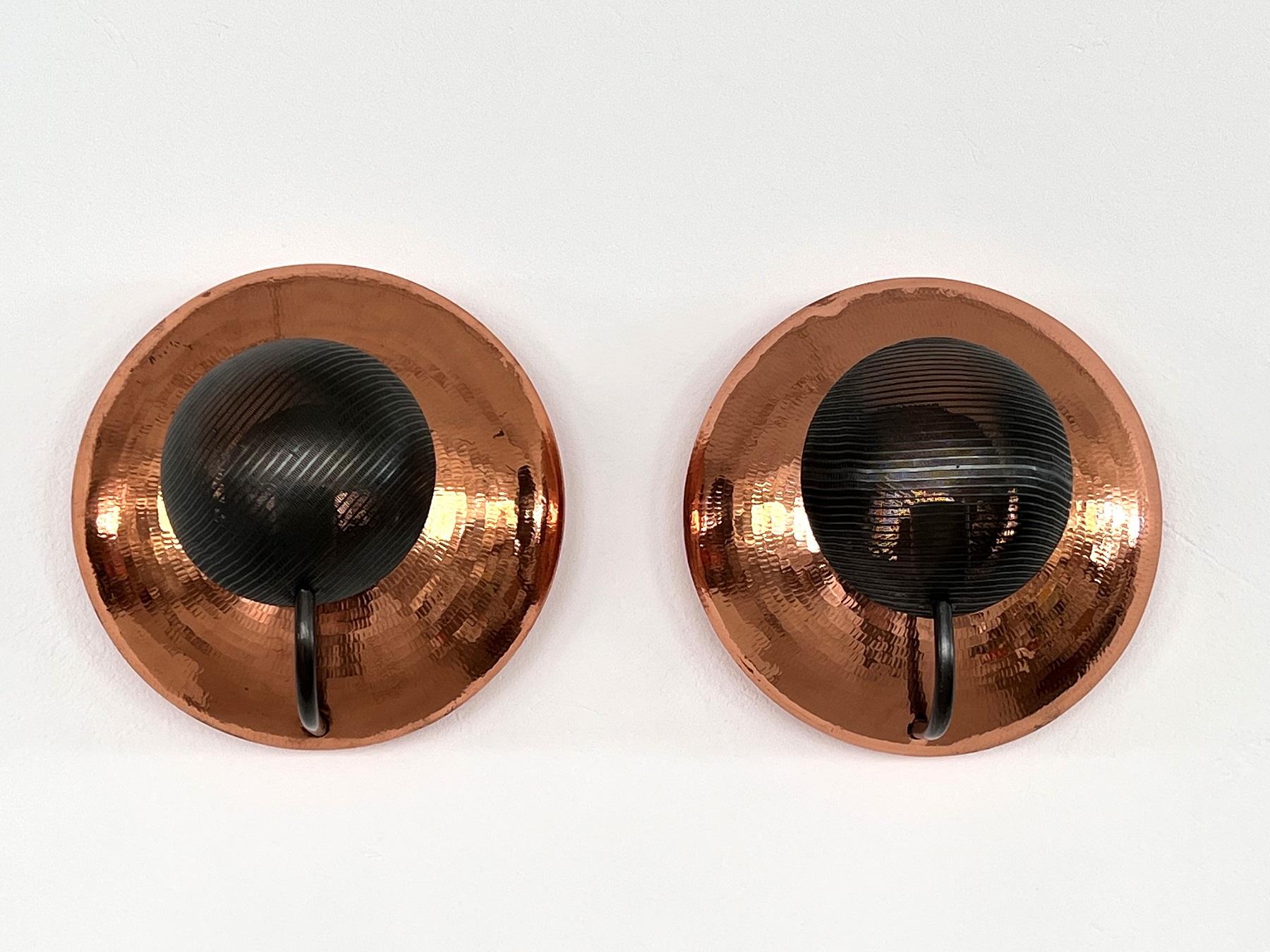Beautiful and particular pair of wall sconces, made of hammered copper and perforated black metal.
Made in Italy in the 1970s.
Both are hollow inside, with a domed shape.
The black metal arms that curve and end in front of the lamps with a