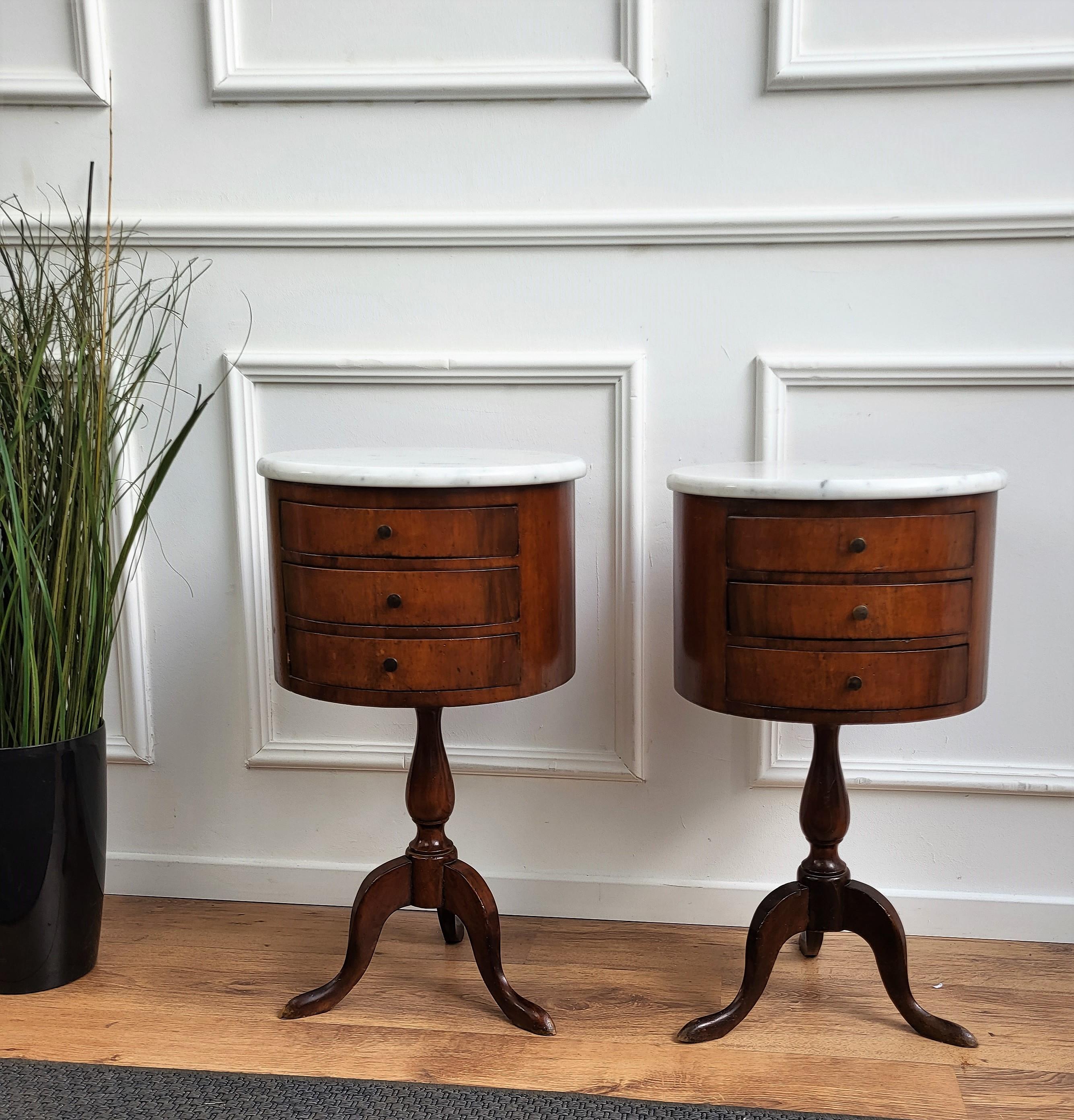 Paire de tables de chevet néoclassiques italiennes très élégantes et raffinées avec une belle structure en bois de noyer, trois tiroirs frontaux et un plateau en marbre blanc de carrare biseauté reposant sur des pieds tripodes classiques sculptés.