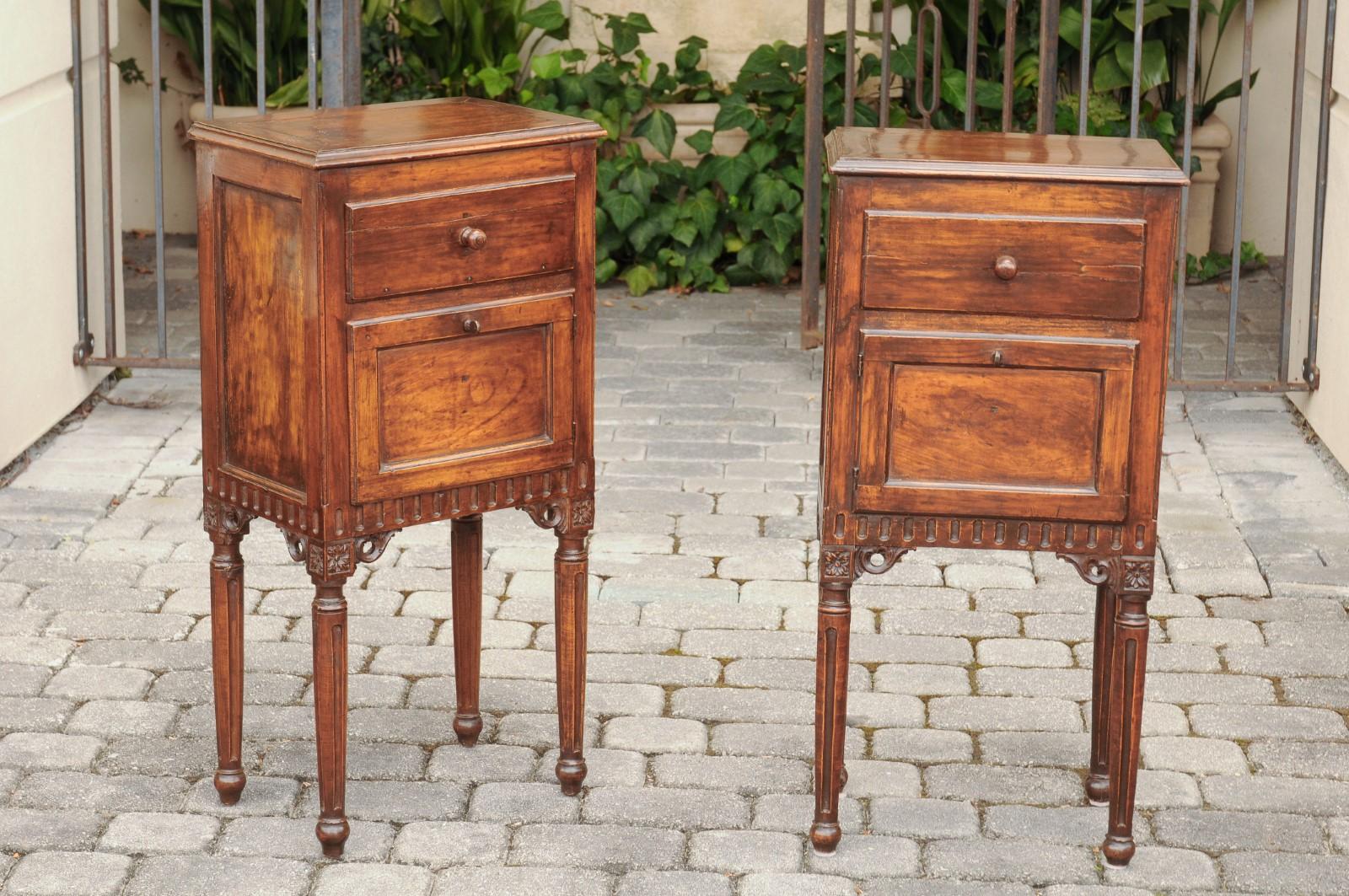 A pair of Italian neoclassical style walnut side tables from the mid-19th century, with door, drawer and carved skirt. Born in Italy during the third quarter of the 19th century, each of these elegant side tables features a rectangular top with