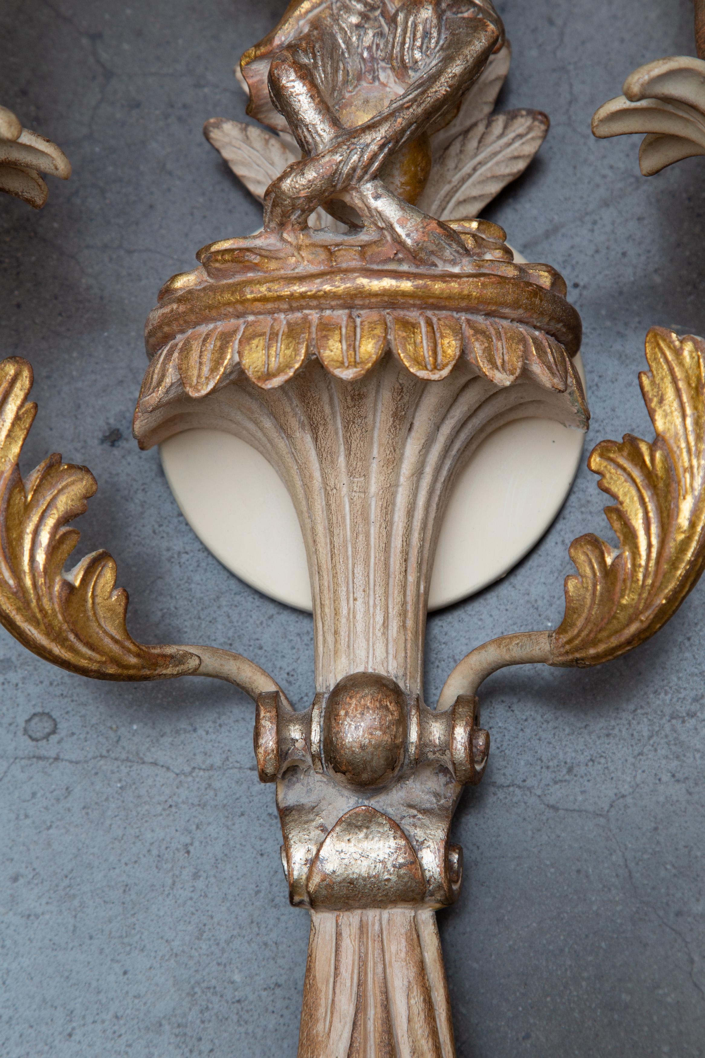 This is an elegant, yet whimsical, set of Italian white-washed beech and parcel gilt two-light sconces, depicting a mirror imaged figural male and female monkey resting under a palm tree.