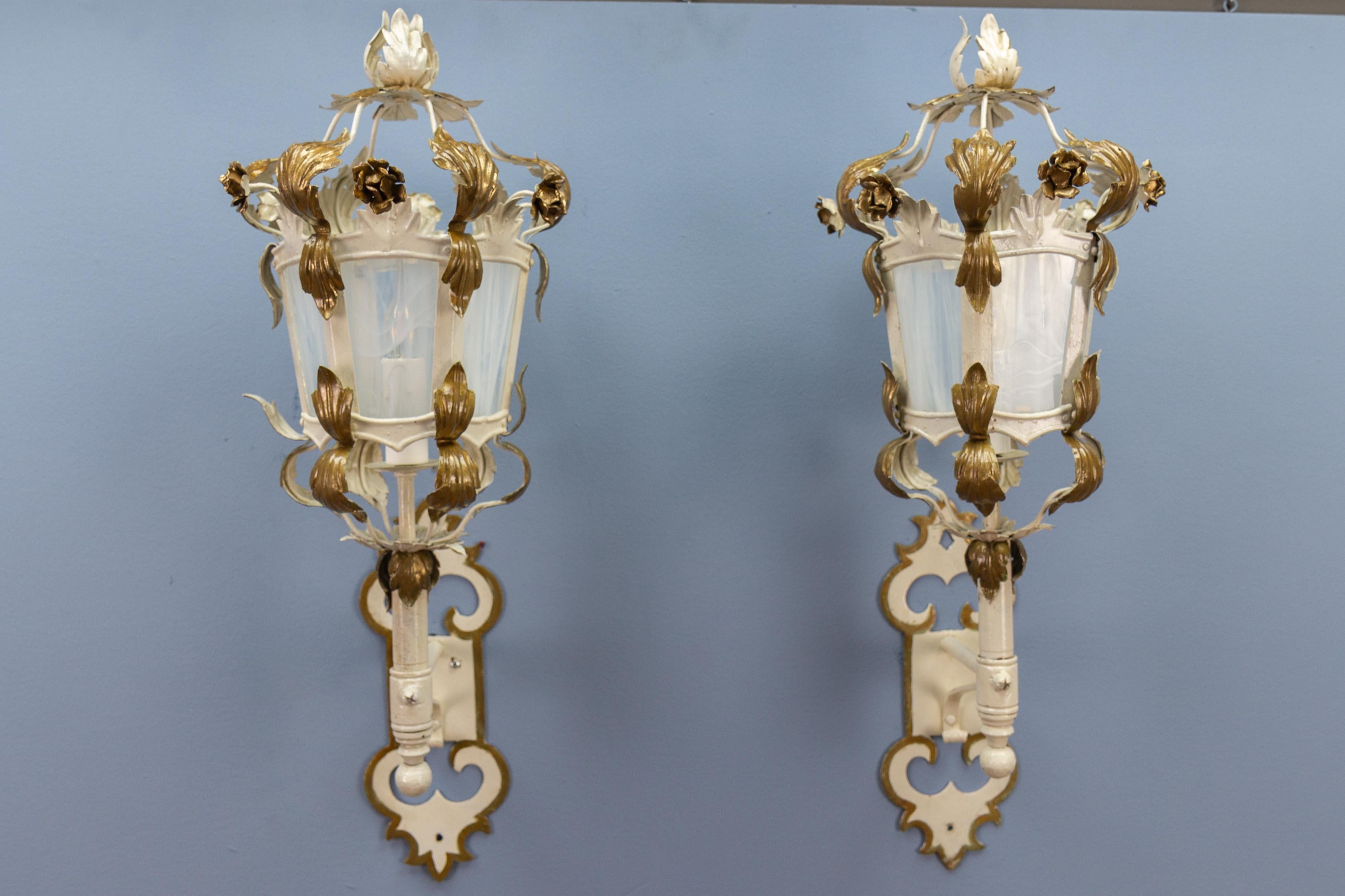 A pair of Italian white and golden color metal and glass wall lanterns from ca. 1970s.
This adorable pair of wall lanterns features a white painted metal frame with golden accents - leaves and flowers. White and partially translucent glass