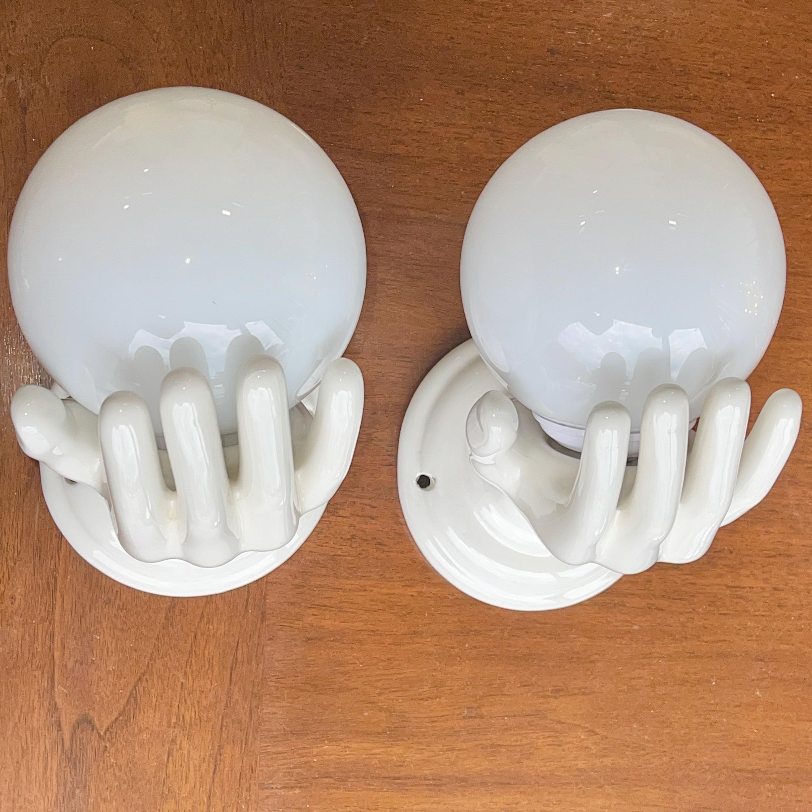 Pair of 1960's Italian white glazed ceramic wall mounted lamps in the form of an open (right) hand holding a white glass globe over a single candelabra socket which holds up to a 60 watt bulb. Can be hard wired or corded.