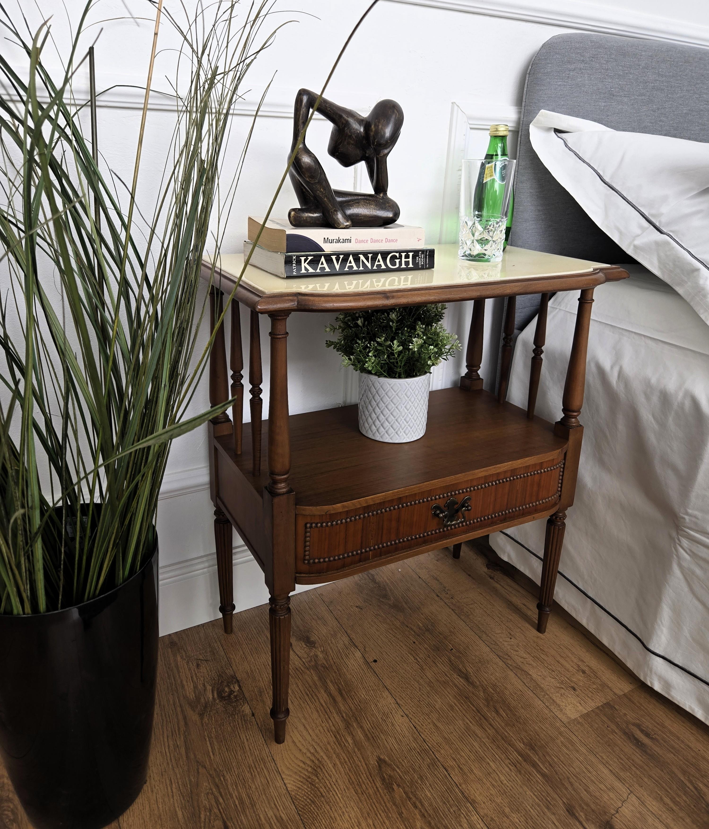 Very elegant and refined Italian 1950s Mid-Century Modern pair of night stands bed side tables in beautiful wooden structure with its framed marble top, decorated carved side columns and feet with open shelf and drawer. Those side tables or