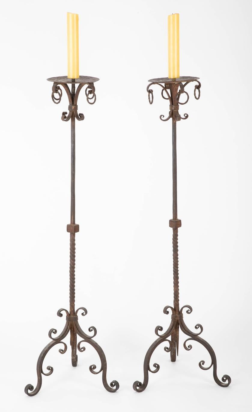 A very handsome and well made pair of hand wrought iron candle holder torcheres with pricket tops. With beautiful details such as the turned shaft, geometric knob with incised decoration, drip pan with twisting iron rings and tripod cabriole legs
