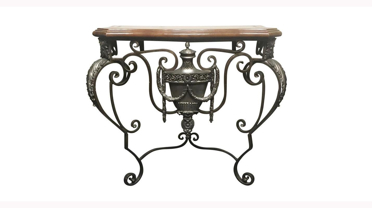 Impressive pair of Italian wrought iron and cast bronze consoles with leather tops.
20th century.

A beautifully tooled brown leather top over a wrought iron scrolling frieze centered by a large neoclassical style carved urn with garlands, raised