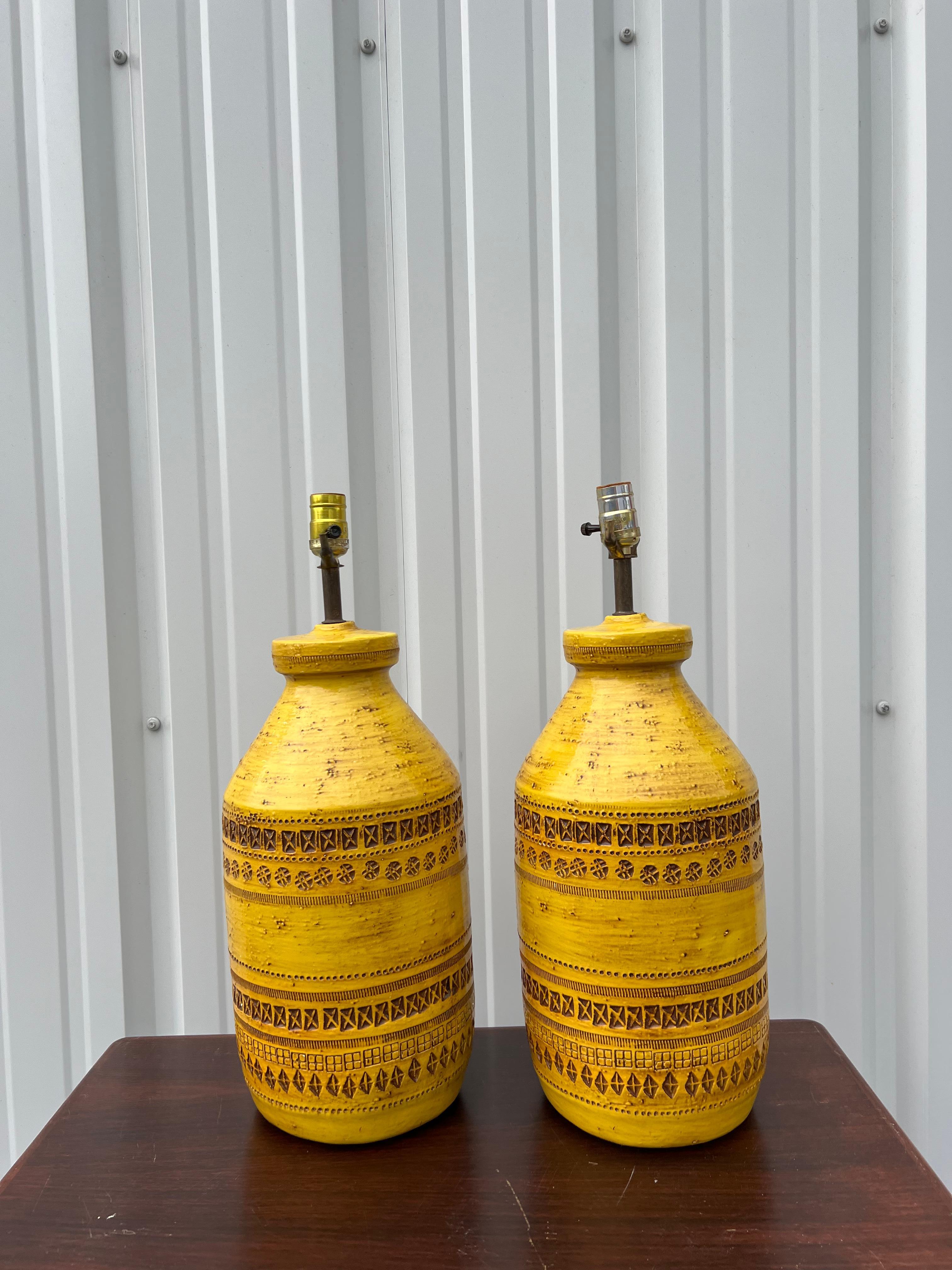 Pair of stunning yellow ceramic lamps with rows of etched patterning manufactured by Aldo Londi for Bitossi. 

Bitossi lamps fuse the decorative with the functional and they are definitely a piece of art! Overall good vintage condition - One lamp