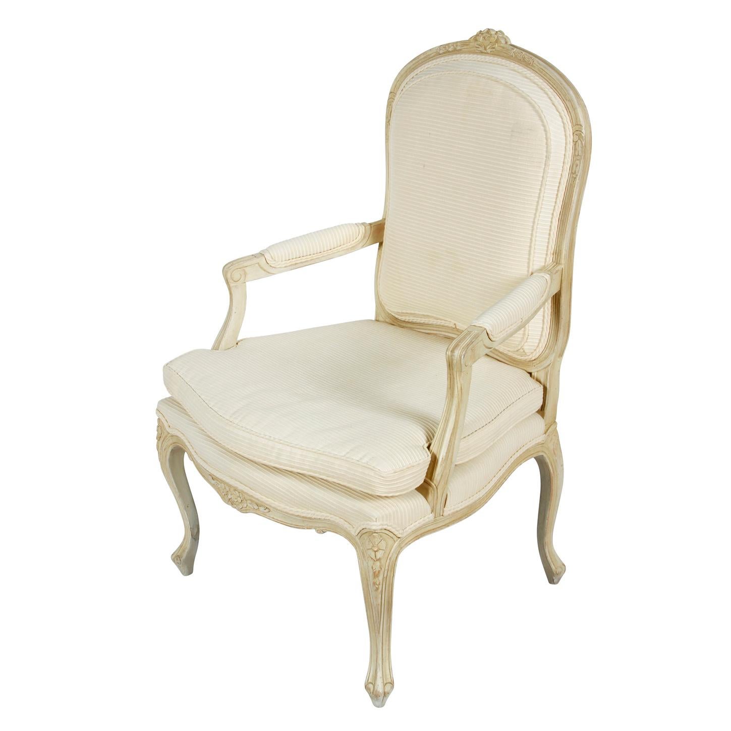 A pair of ivory and painted French bergeres chairs. The Louis XV style arm chairs are painted antique white and carved with floral details at the chair frame back, apron and cabriole legs. The chairs are upholstered in to the back, seat and arm