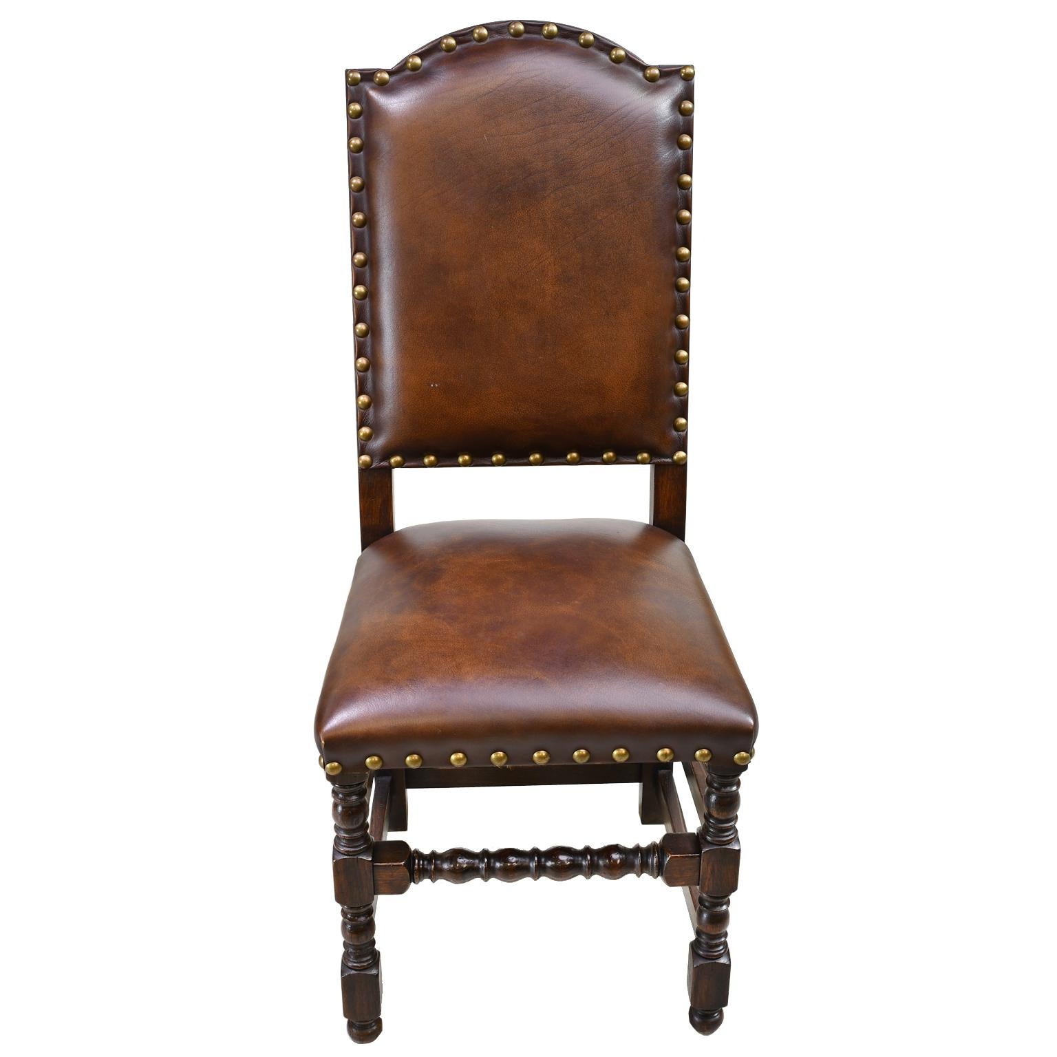 A well-crafted pair of Jacobean or Baroque style dining chairs with dark oak frames with expresso coffee-colored leather upholstery on arched back and seat trimmed with decorative brass nail heads, circa 2000. Chairs are supported on turned front