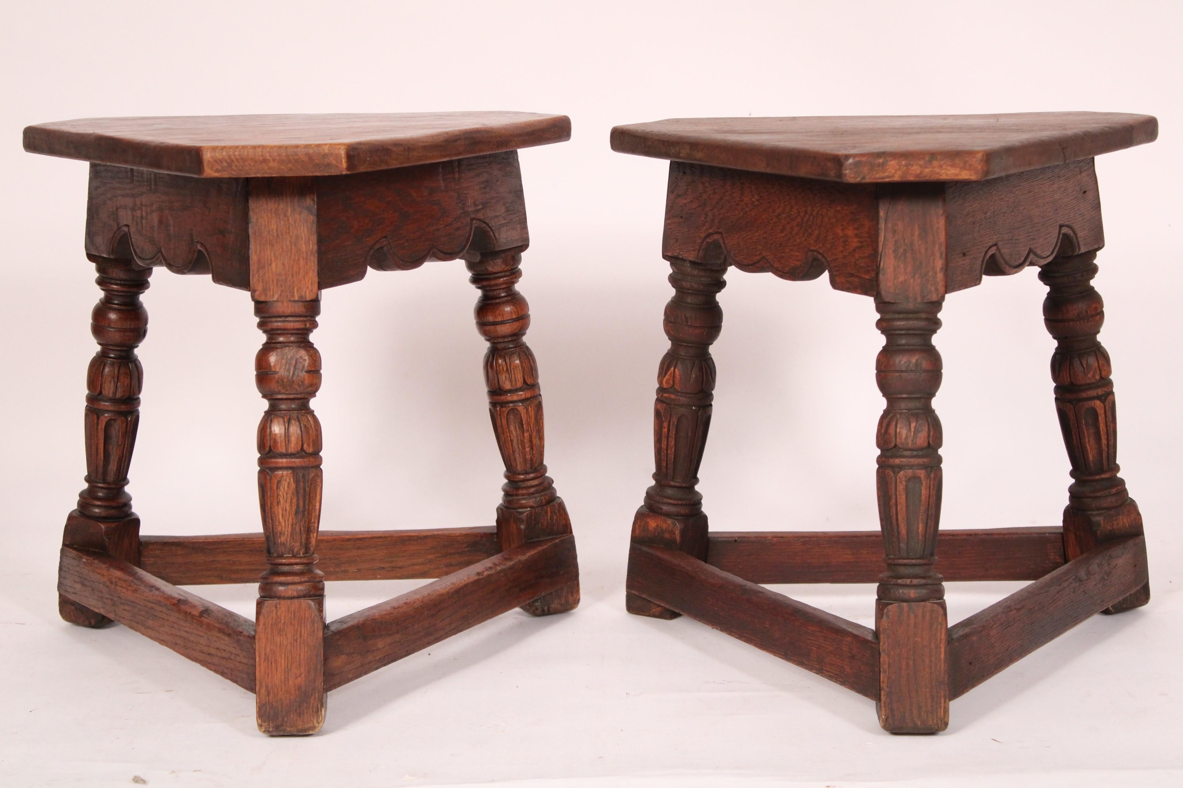 Matched pair of Jacobean style oak joint stools, circa 1930's. Each joint stool with a triangular shaped top with canted corners, 3 turned and carved oak legs joined by stretcher bars. One joint stool bearing a Marshall Laird metal plaque. One or
