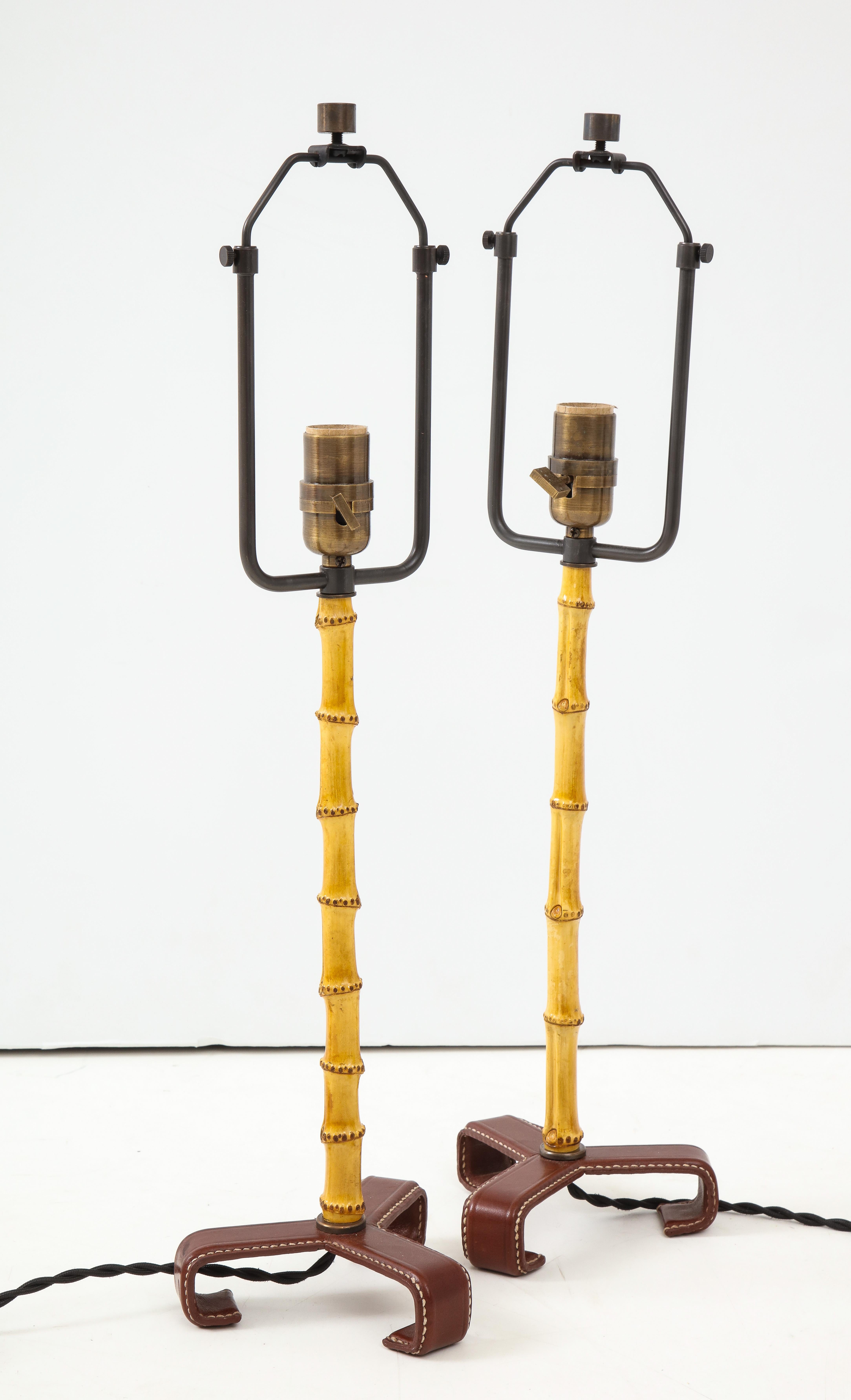 Exceptional pair of Jacques Adnet table lamps from France, c. 1950s. Elegant composition includes a stitched leather tripod base, natural bamboo body, and brass socket.  

Sold as a pair.