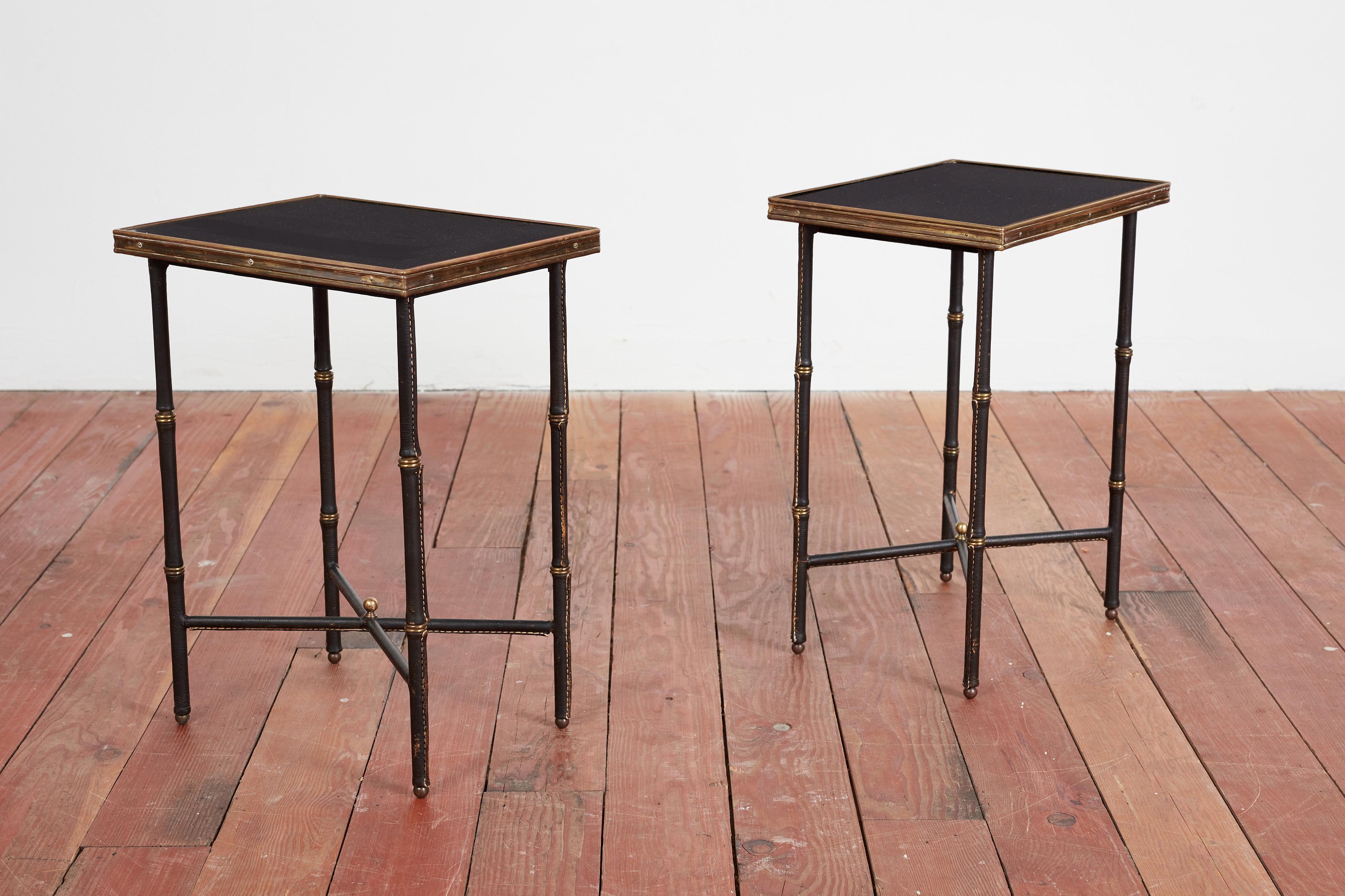 Pair of Jacques Adnet end tables with original bamboo leather legs with contrast stitching and brass feet. 

Petite in scale - with brass edging with just the right patina. 

France, circa 1940s