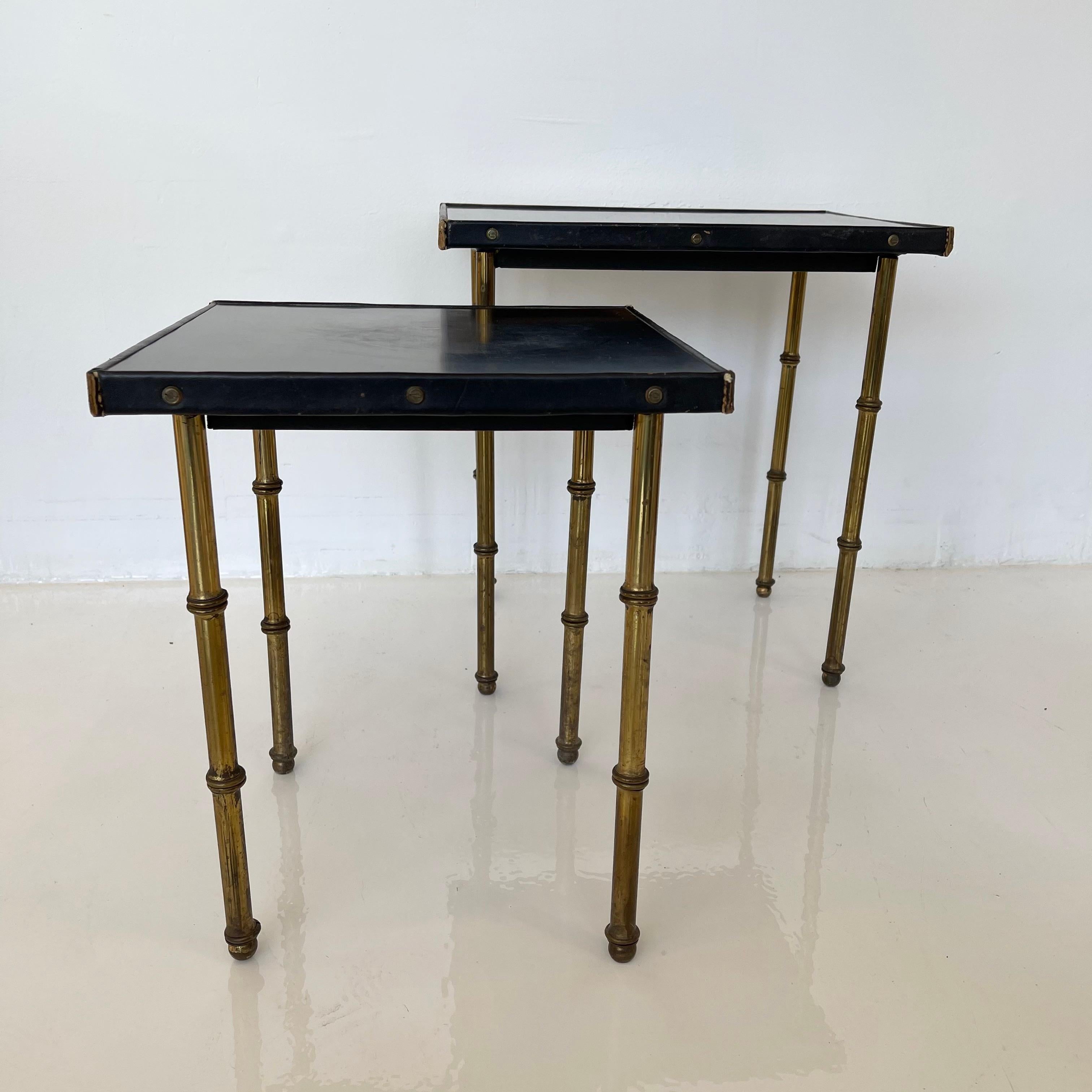Handsome pair of side tables by Jacques Adnet. Brass bamboo legs, black Masonite top with leather trip and brass hardware. Iron frame. Very good vintage condition. Smaller table can nest perfectly underneath the larger table. Rare set of collectible