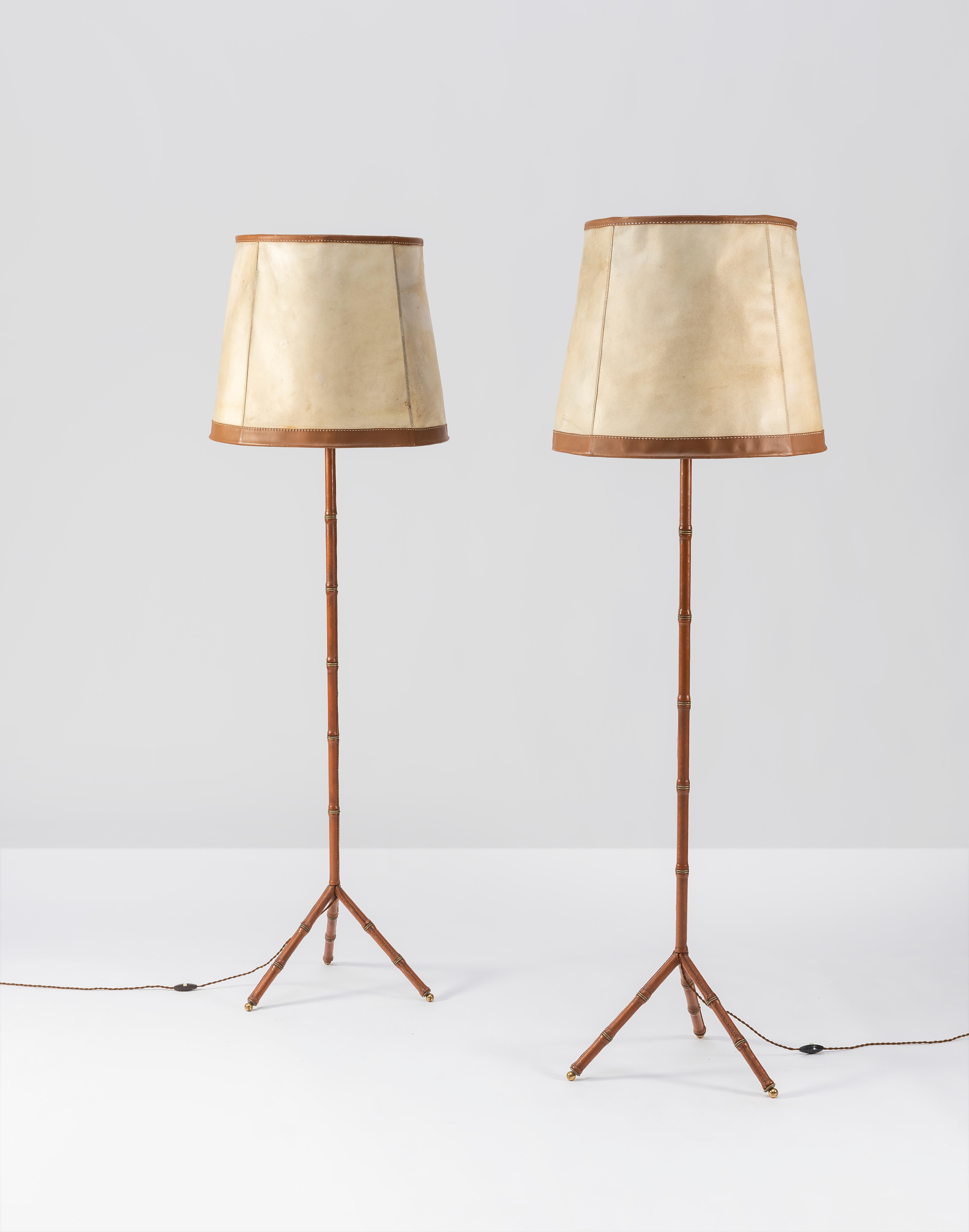 Rare pair of Jacques Adnet hand-stitched leather bamboo floor lamps with original leather and parchment shades. 

Leather with beautiful age-appropriate patina. 

Some dimpling to parchment on shades.