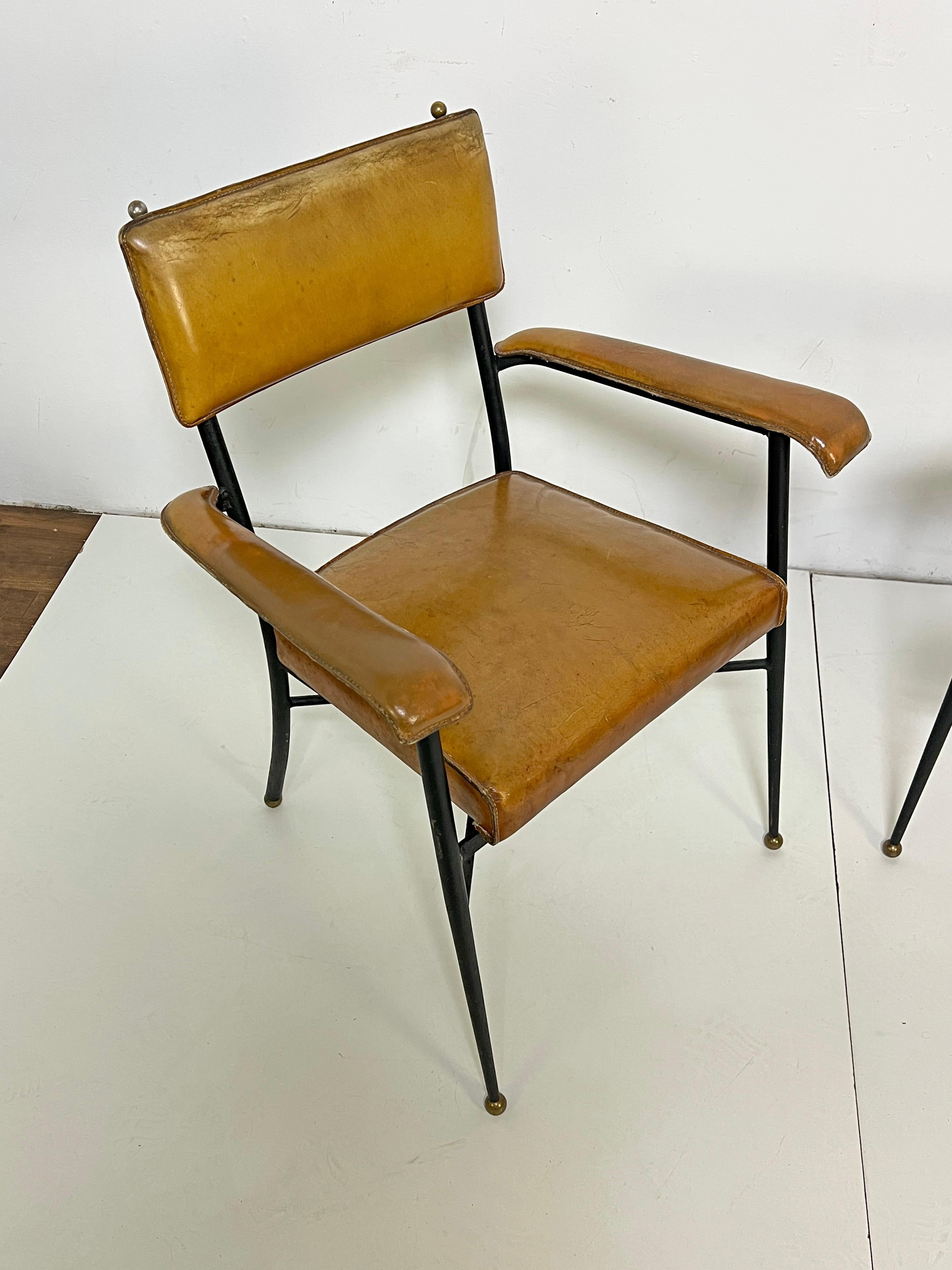Pair of steel framed armchairs by Jacques Adnet, ca.  late 1940s. These are covered in their original saddle tanned and stitched leather and subtly accented with bronze pommels and feet. 