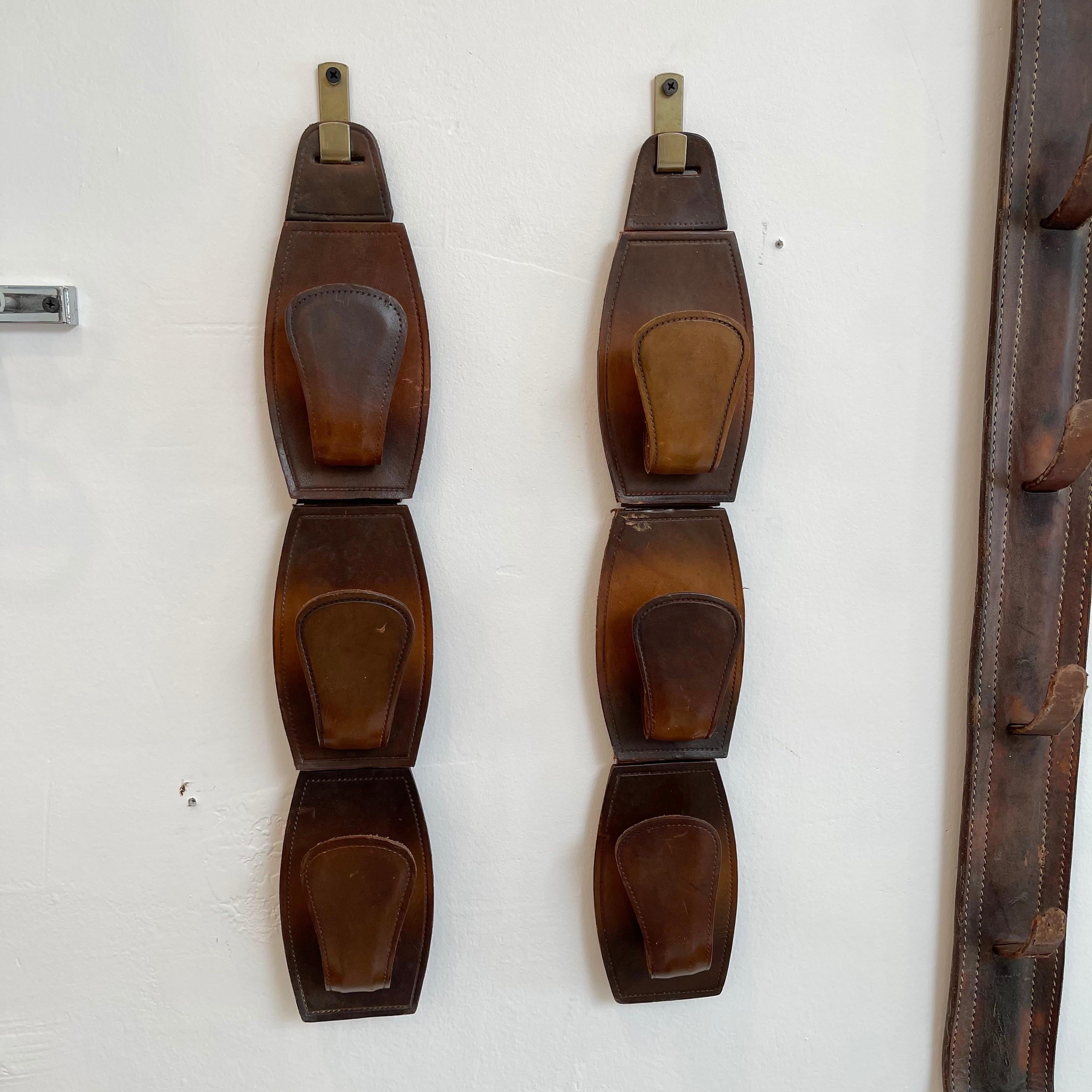 Great pair of French saddle leather hooks in the style of Jacques Adnet. Brass wall hook with leather hooks hanging from bracket. Each set has three individual hooks that are joined on the backside. Beautiful saddle leather with rich patina. Hooks