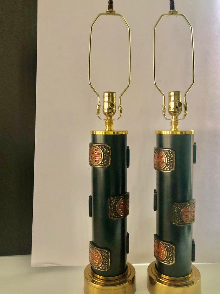 Pair of vintage table lamps in the style of James Mont that are beautifully made, quite heavy, having a black matte finish decorated with metal Asian inspired medallions in black, red and gold. The tops and bottoms are finished with brass cuffs. The