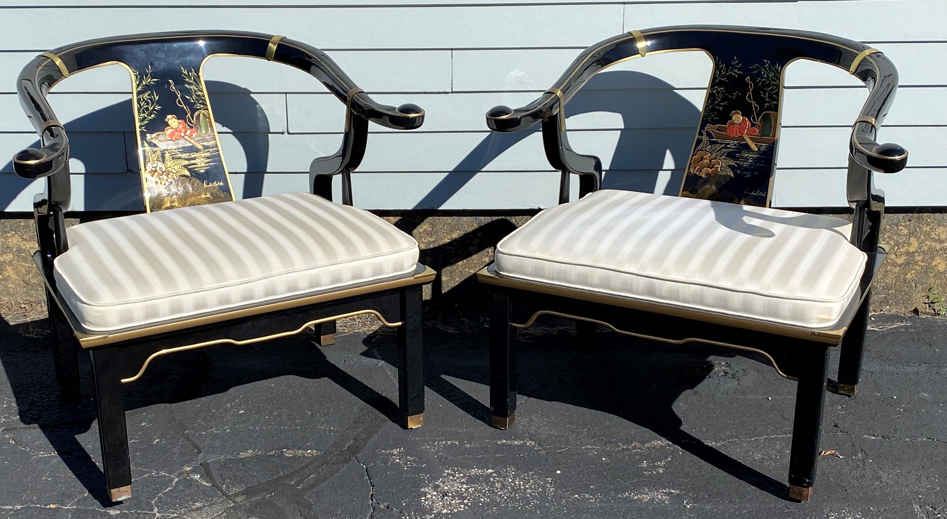 A stunning pair of James Mont style black lacquer Chinese horseshoe chairs with polychrome hand painted Asian scene splats by Brenda Bolick, gilt line highlights, brass corner, arm, and foot supports, and white satin striped upholstered seats. A