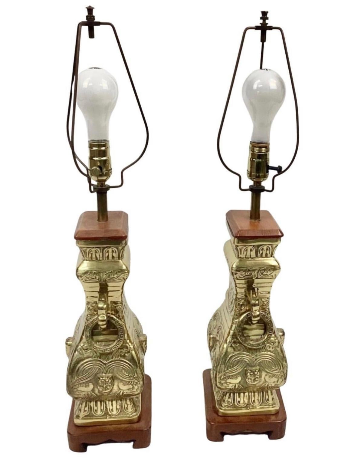 Pair of impressive 20th century chinoiserie brass table lamps in the style of James Mont. Solid brass with a wooden base and cap. Ornate brass rings hang from either side of lamps.

Dimensions:
26.5