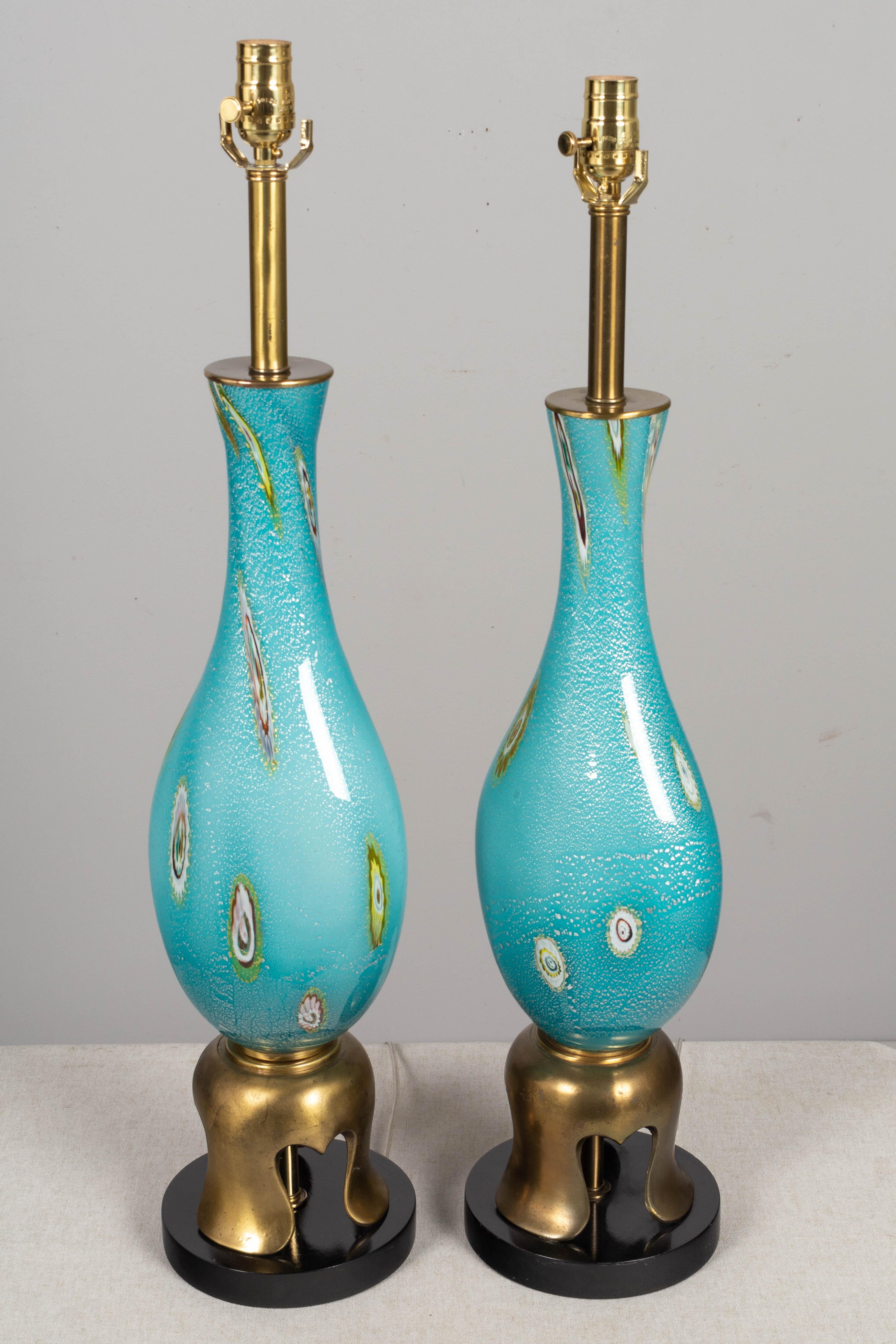 A pair of Mid Century Murano art glass table lamps by Barovier & Toso. Hand blown aqua blue glass with colorful murrines and silver foil. Original gold tone cast metal and black lacquered wood bases, in the style of James Mont. Red foil label on one