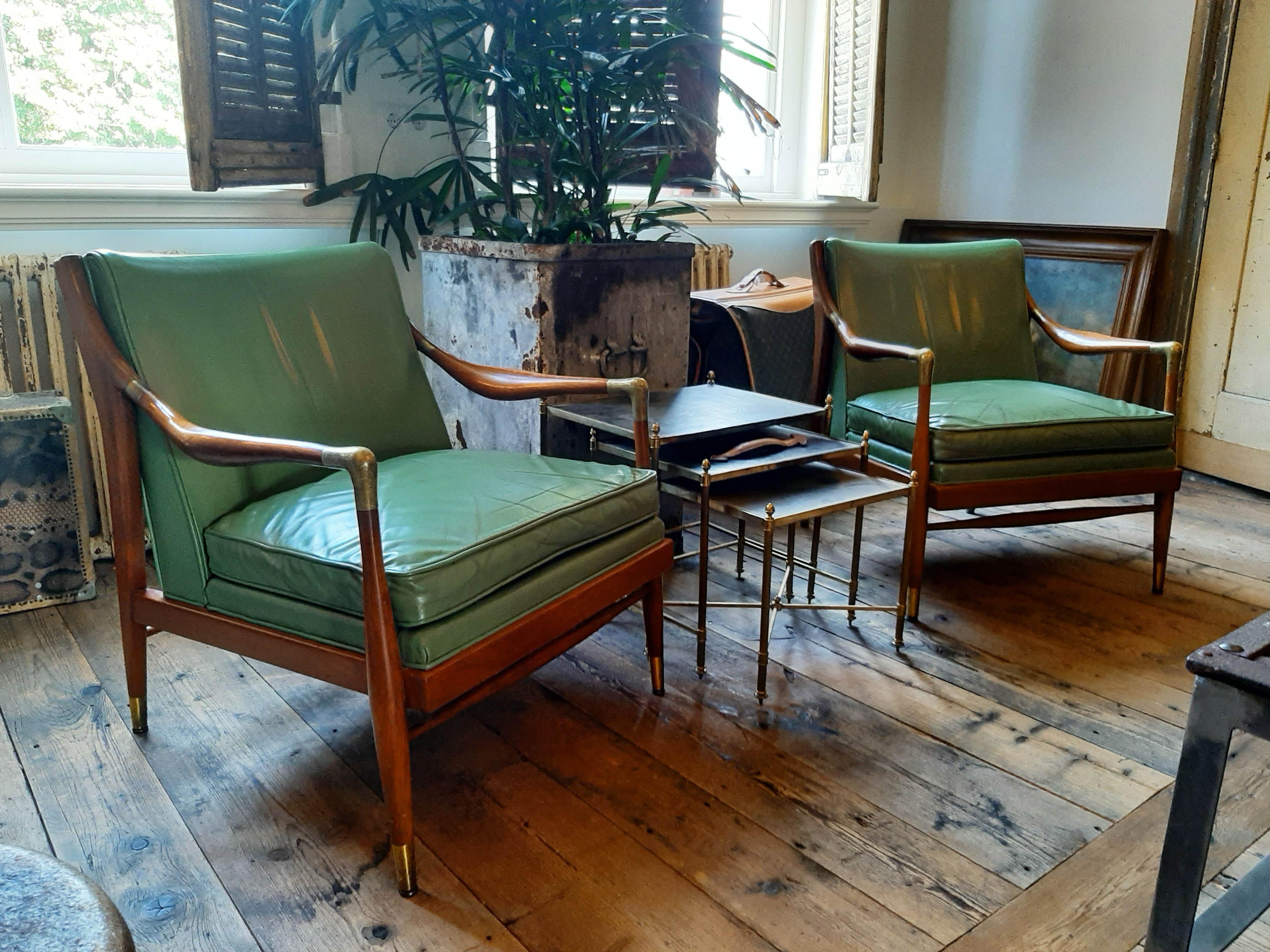 A 1950s pair of sculptural open armchairs in the manner of Gio Ponti. With original green leather upholstery, studded on the back. The walnut frame has solid brass armrest elbows and brass sabots, by Jamestown Royal. 

The seat height is 44 cm en