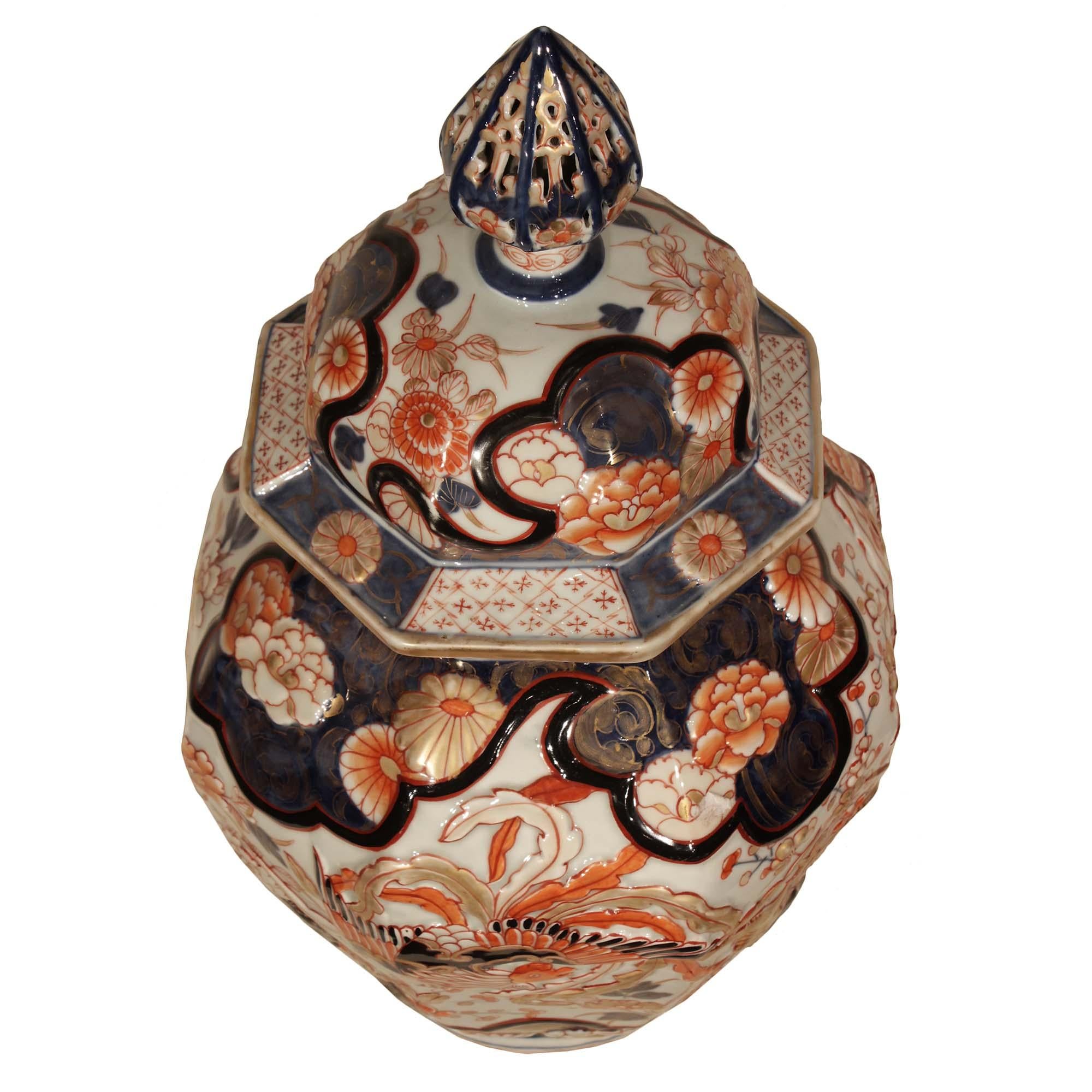 An impressive and true pair of 19th century Imari lidded urns. Each octagonal urn is decorated with protruding hand painted richly hued floral patterns with the mythical Phoenix at the center. The top lip is decorated with alternating clover