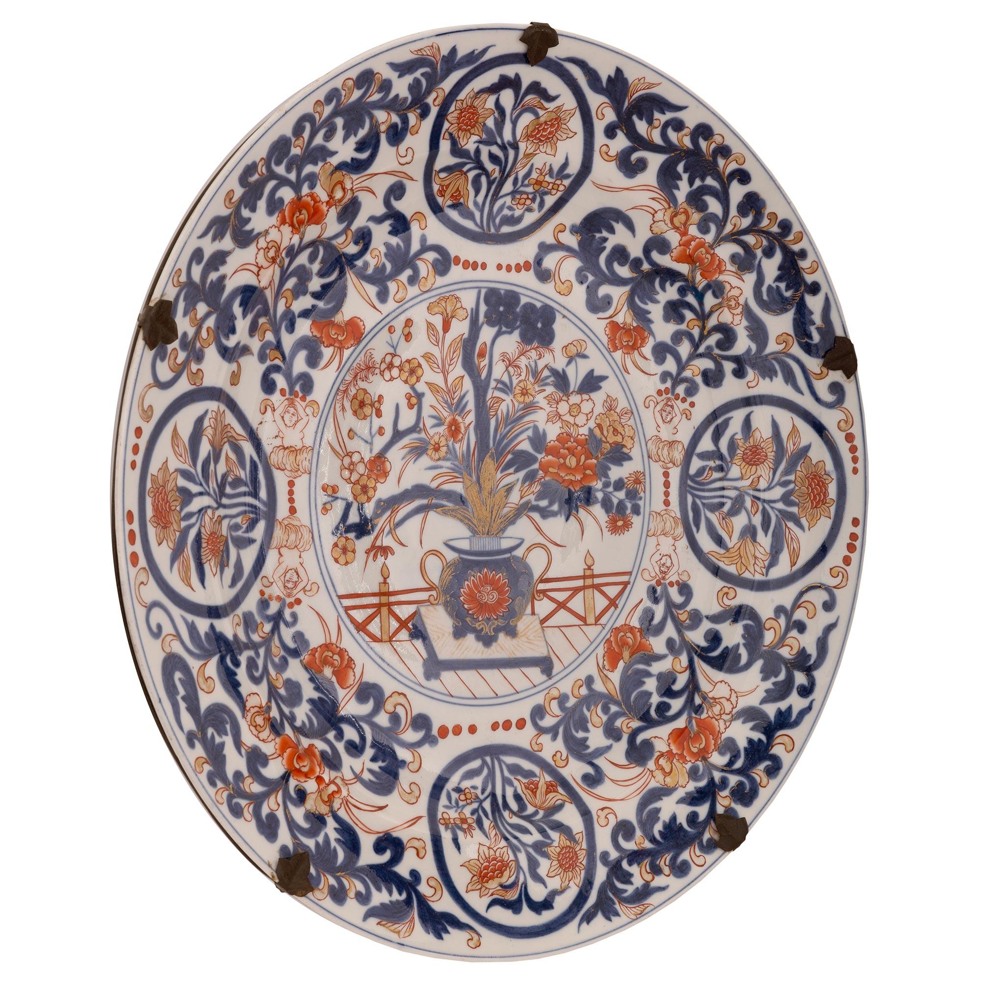 A beautiful and most decorative pair of Japanese 19th century Imari porcelain plates. Each circular plate displays striking finely detailed scrolled foliate designs with flowers in an urn at the center in the traditional red and blue colors with