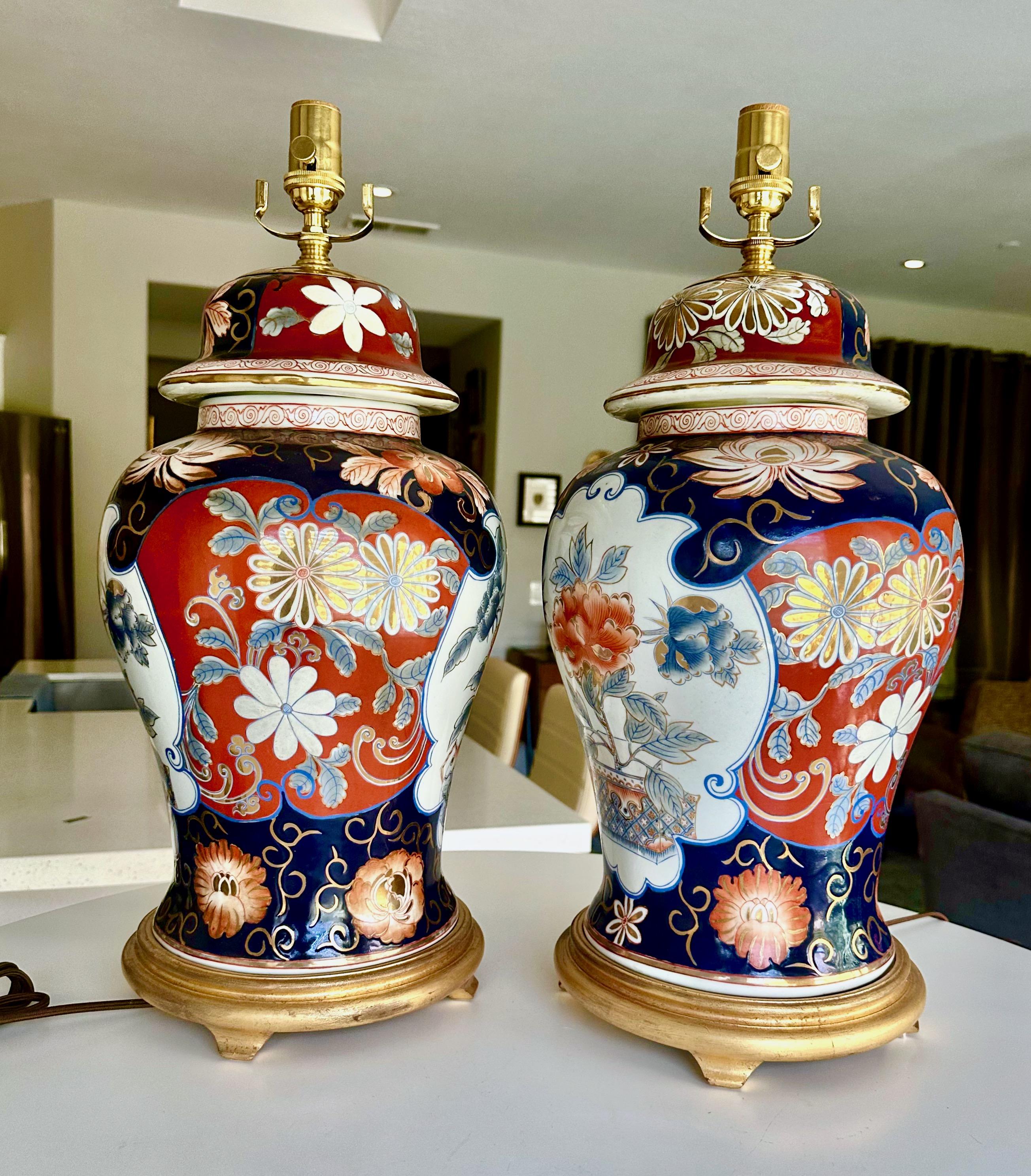 Paire de vases en porcelaine japonaise Imari en forme de pots de gingembre montés sur des bases en bois doré. Les couleurs sont celles de l'Imari classique, dans des tons riches d'orange brûlé et de bleu foncé, rehaussés d'or. Le motif comprend des