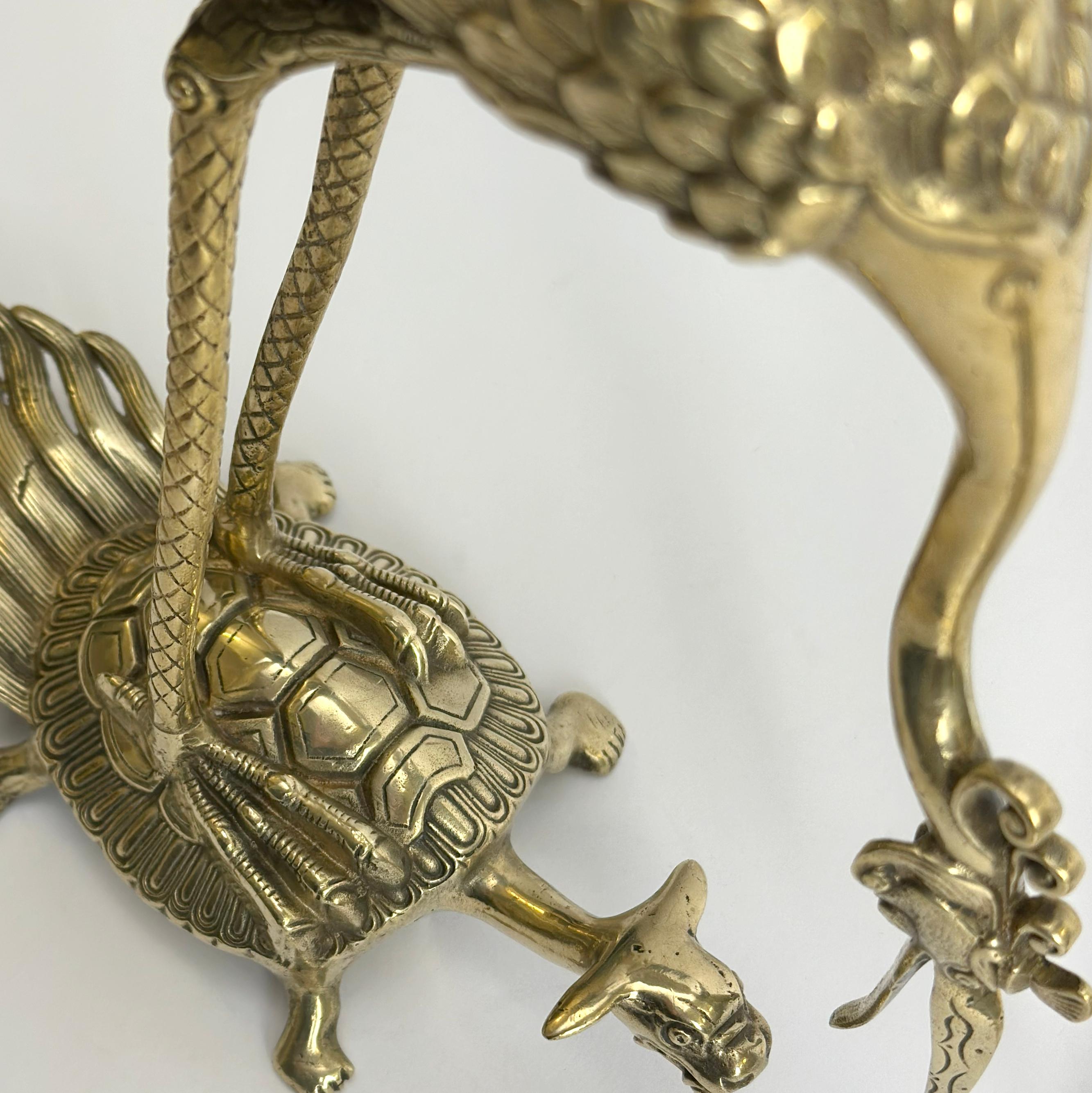 A pair of Japanese decorative brass crane sculptures, offering a striking interpretation of traditional symbolism in cast metalwork. Each brass crane, rendered with elegant lines and a slightly stylized form, is perched upon a turtle—an iconic motif