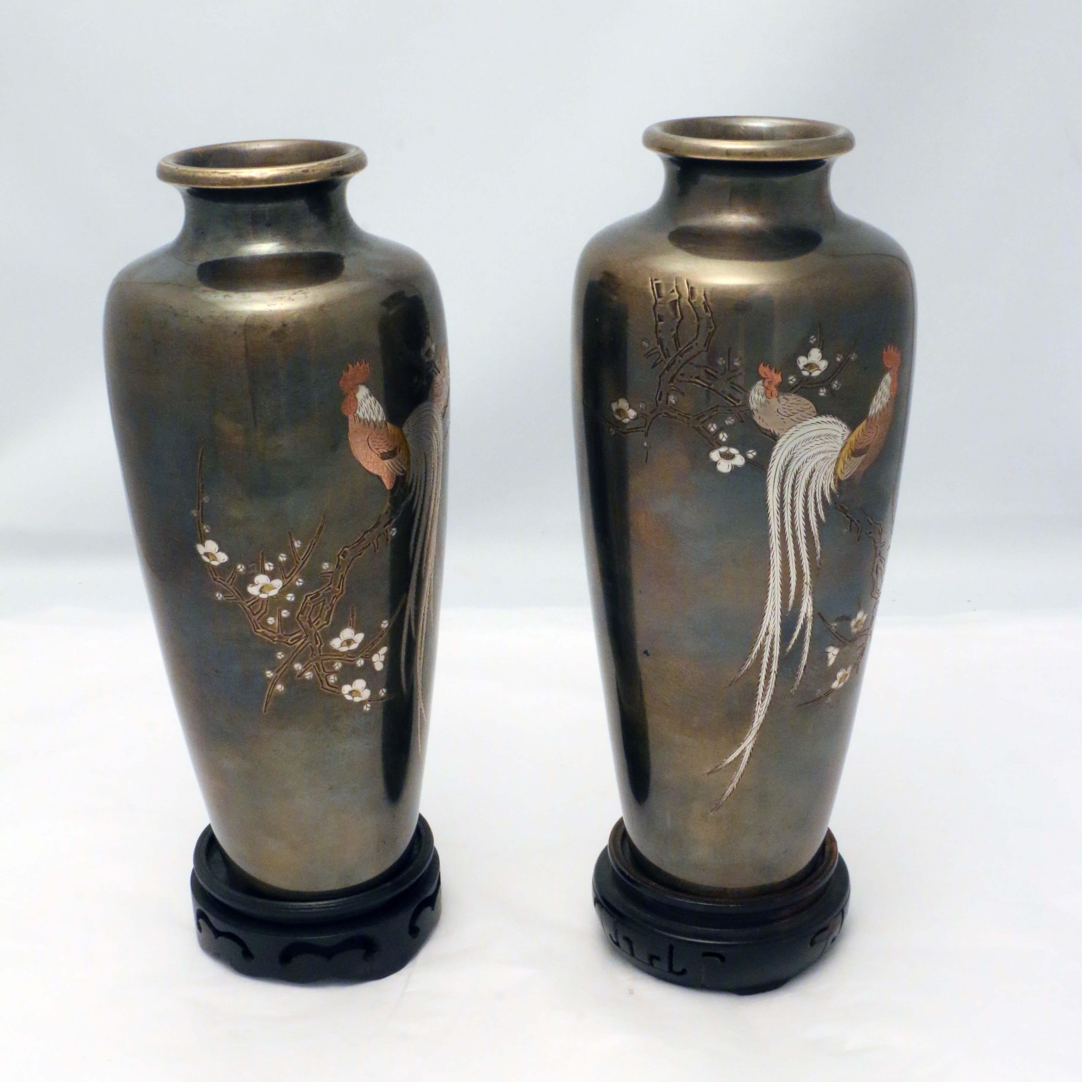These slender vases are hand engraved with a cock roosting on a prunus branch, while the hen sits in the background. The decorator has given him a long feathery tail like a bird of paradise. The coxcomb and body are colored with a wash. They are a