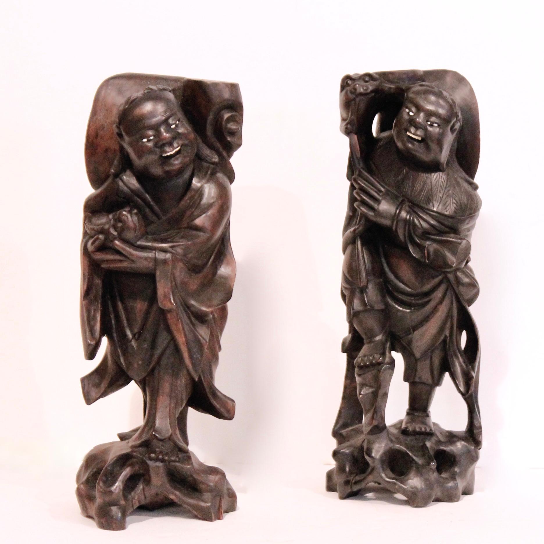 An unusual pair of  sculptural candle or joss stick holders- a pair of jolly grinning men holding up smiling fish and standing on stylized rockery bases carved of a piece with the rest. Each figure is carved in three dimensions. The backs, while