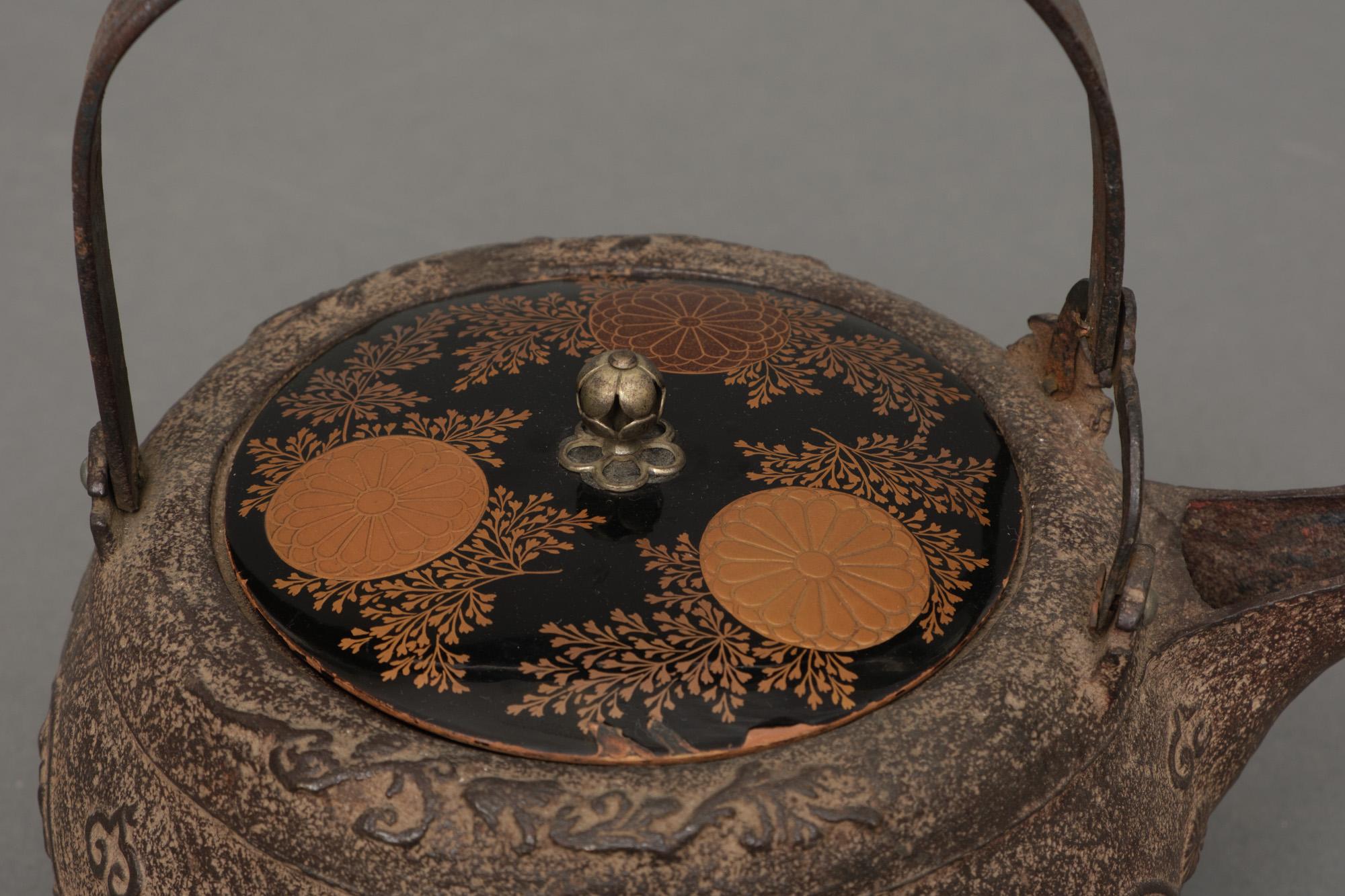 Pair of enticing cast iron chôshi (sake kettles) with a detailed lacquered lid, raised by three low feet. Its rotund body with a subtle embossed design of stylized symbols, like mythical creatures in cartouches, Buddhist flames and chrysanthemum