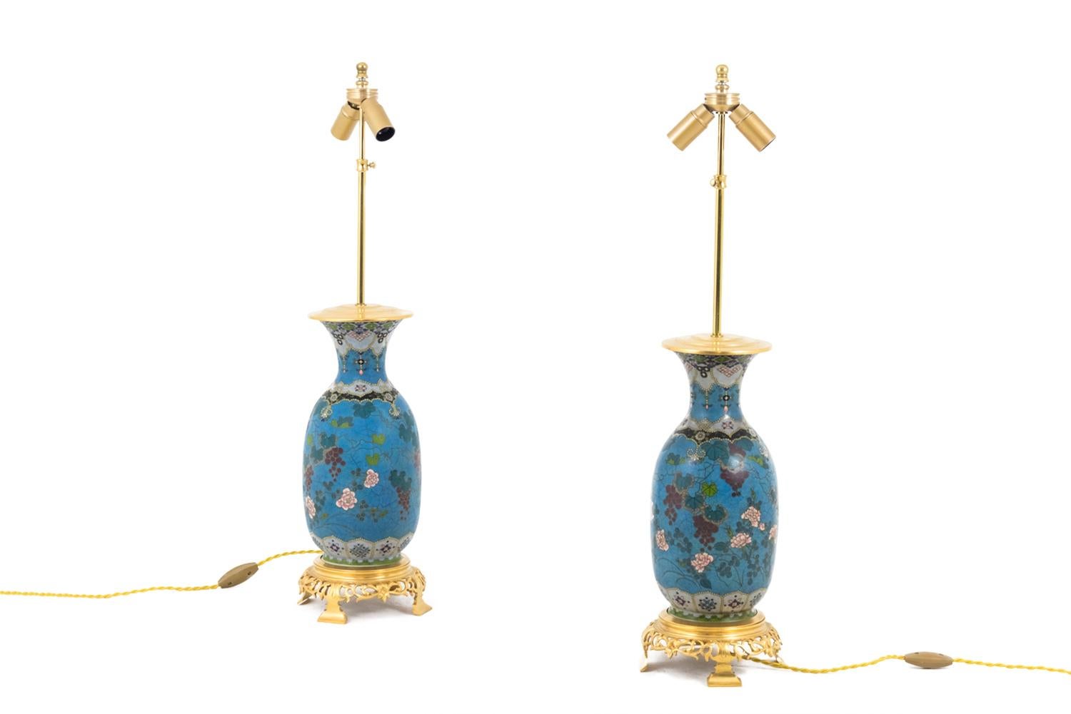 Pair of Amphora shaped Japanese porcelain lamps in cloisonné enamel and chiselled and gilt bronze mount, standing on a gilt bronze circular quadripod base with an openwork decor of foliage scrolls.
Body of the lamp in cloisonné enamel with a blue