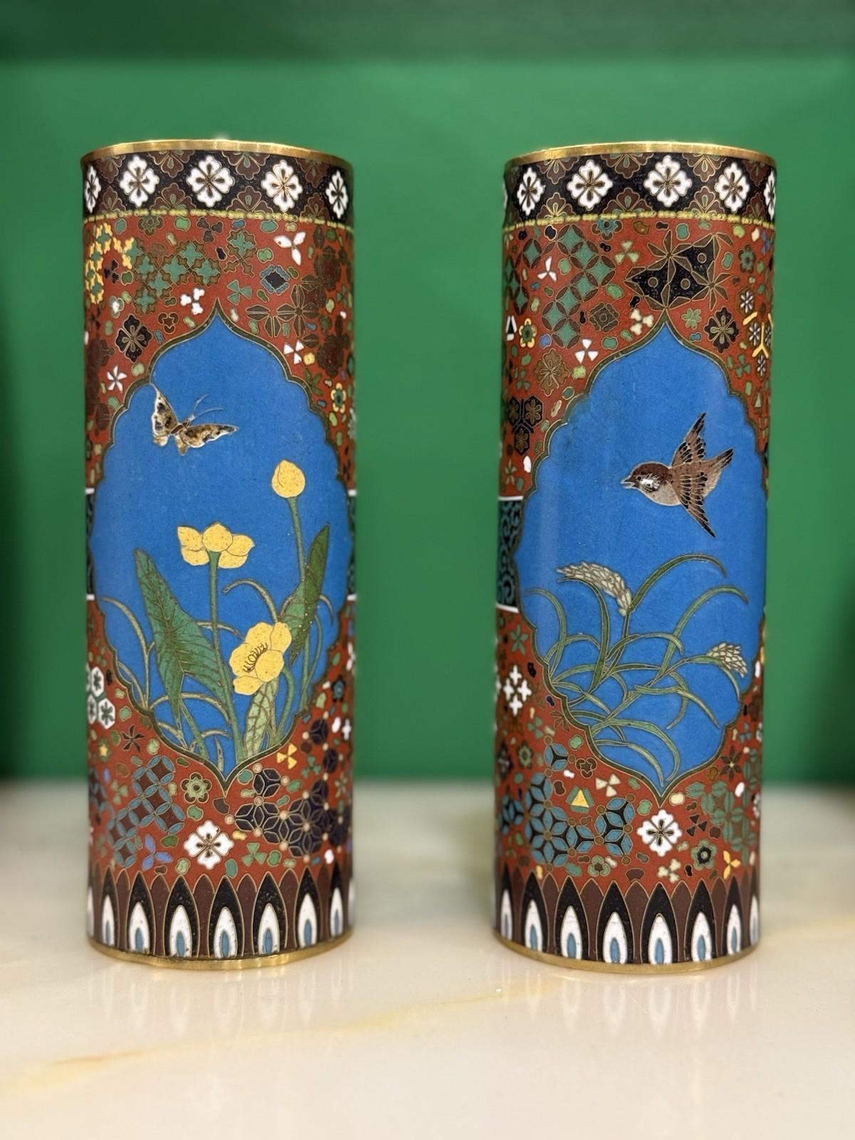 A refined pair of Japanese Meiji-period cloisonné enamel vases, worked in the manner of Gotō Seizaburō. Each cylindrical vase displays two shaped reserves set against a vivid turquoise-blue ground: one depicting a sparrow in flight above grasses,