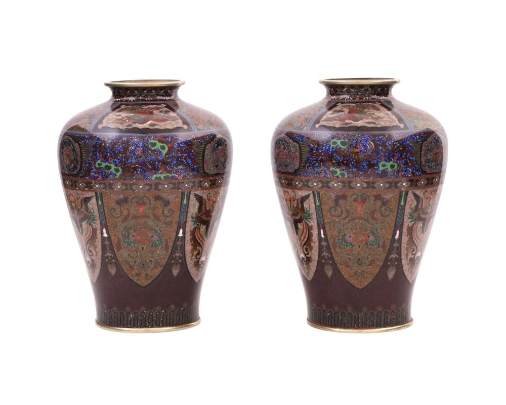 A pair of rare identical antique Japanese Meiji era enamel vases. The amphora shaped vases are adorned with polychrome enamel panels depicting symmetrical images of Phoenix birds, qilins, and dragons surrounded by floral, and foliate scroll motifs