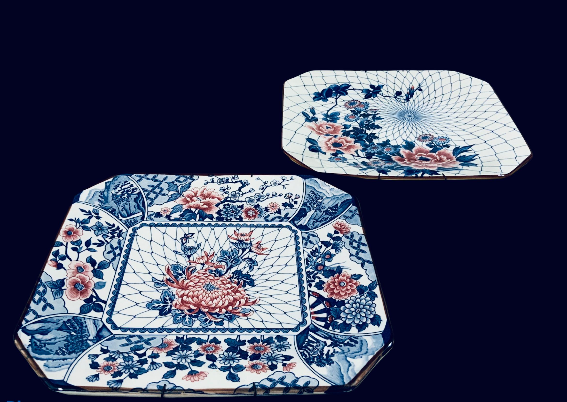 Dies ist ein Paar japanischer handbemalter MCI-Porzellan-Wandteller. Sie haben eine achteckige Form und sind in blauen, roten und rosa Farben auf weißem Hintergrund gemalt. Beide zeigen ein zentrales Bouquet aus großen Blumen und Blättern vor einem