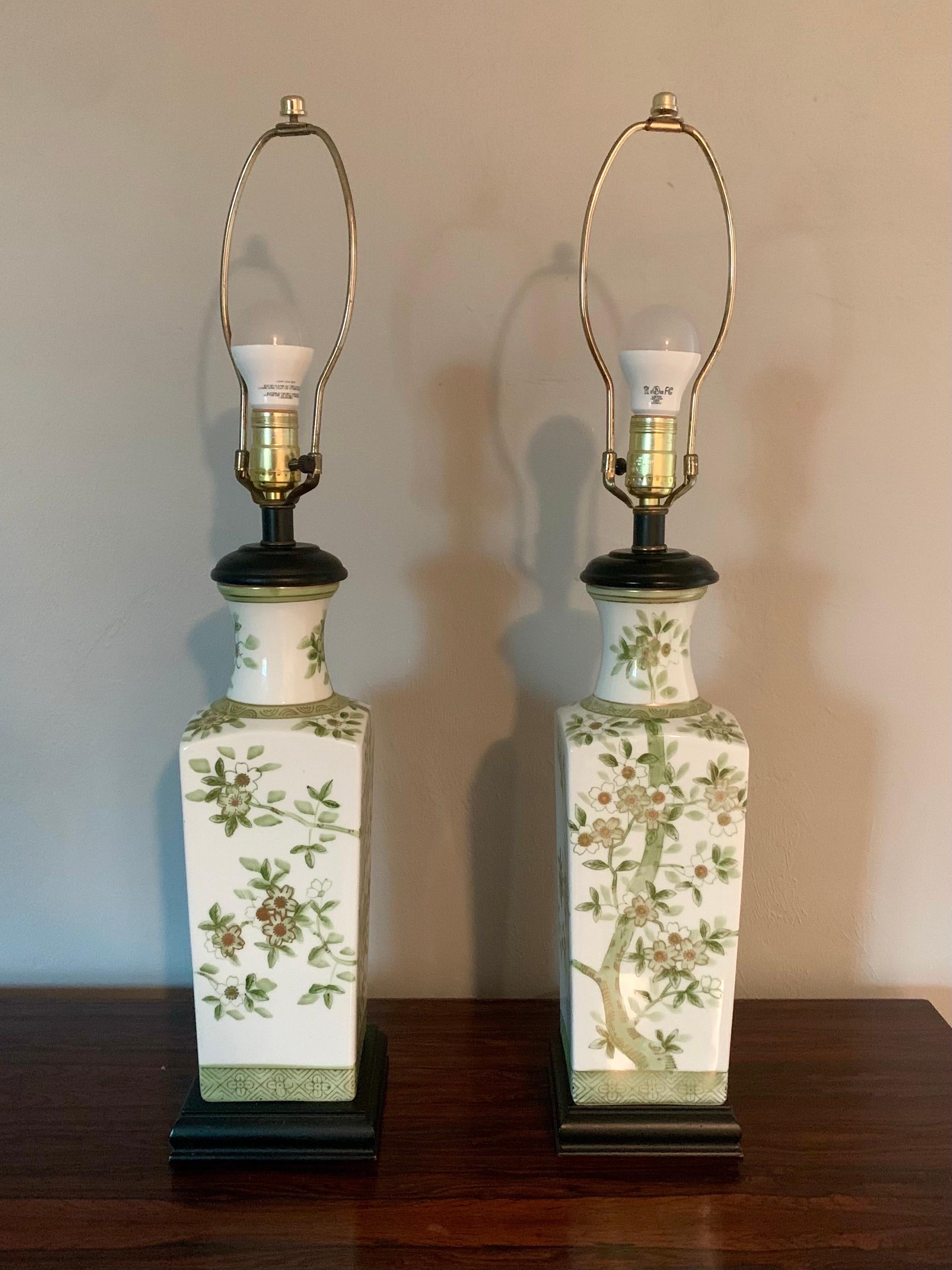 Pair of elegant porcelain lamps from Japan. Circa 1940s - 1950s. A glossy white vase. Adorned by images of cherry blossoms on all sides. Hand painted with various tones of green and gold. 

Black wooden base. 

Sold with out shades.