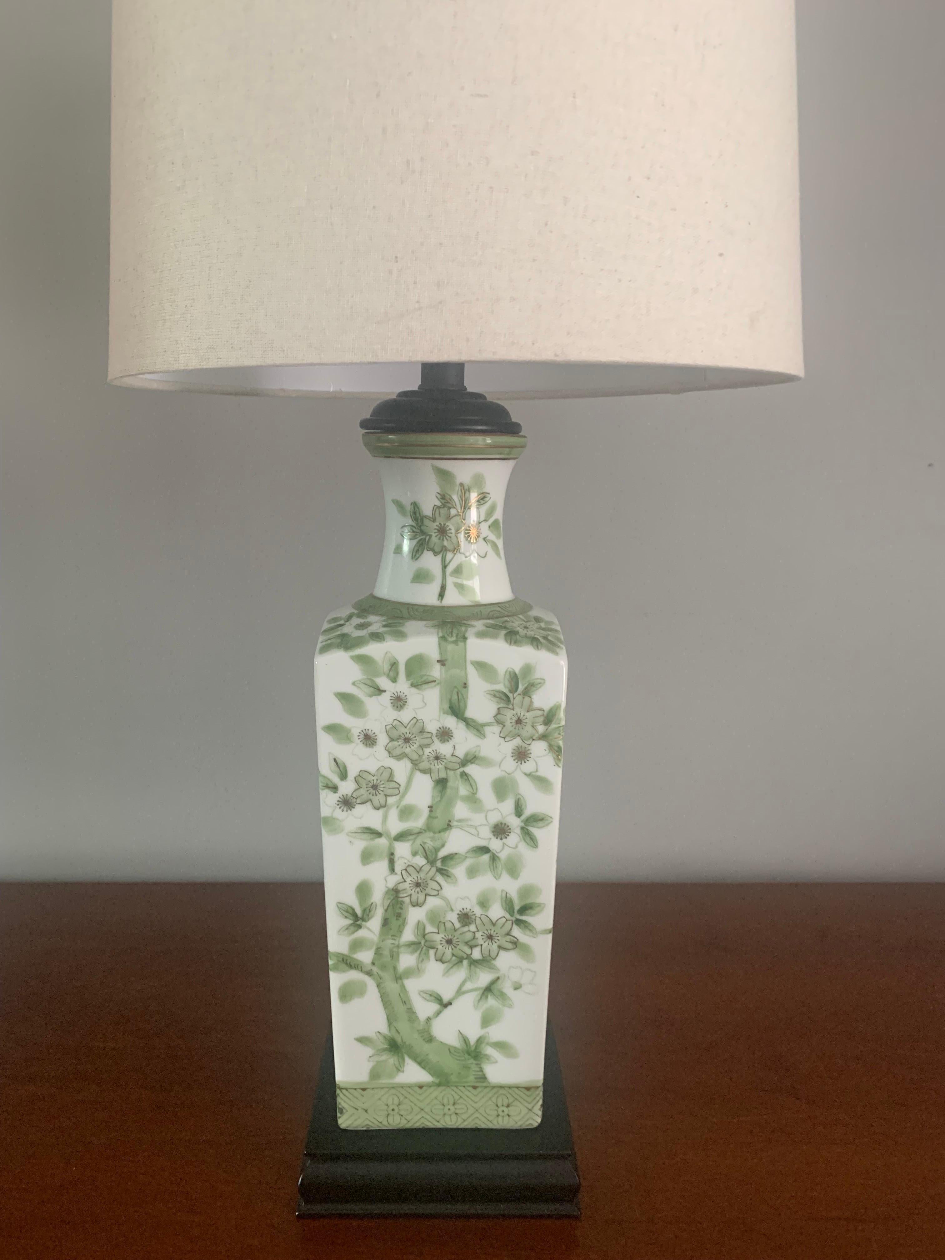 Pair of elegant porcelain lamps from Japan. Circa 1940s - 1950s. A glossy white vase. Adorned by images of cherry blossoms on all sides. Hand painted with various tones of green and gold. 

Black wooden base. 

Sold with out shades. 