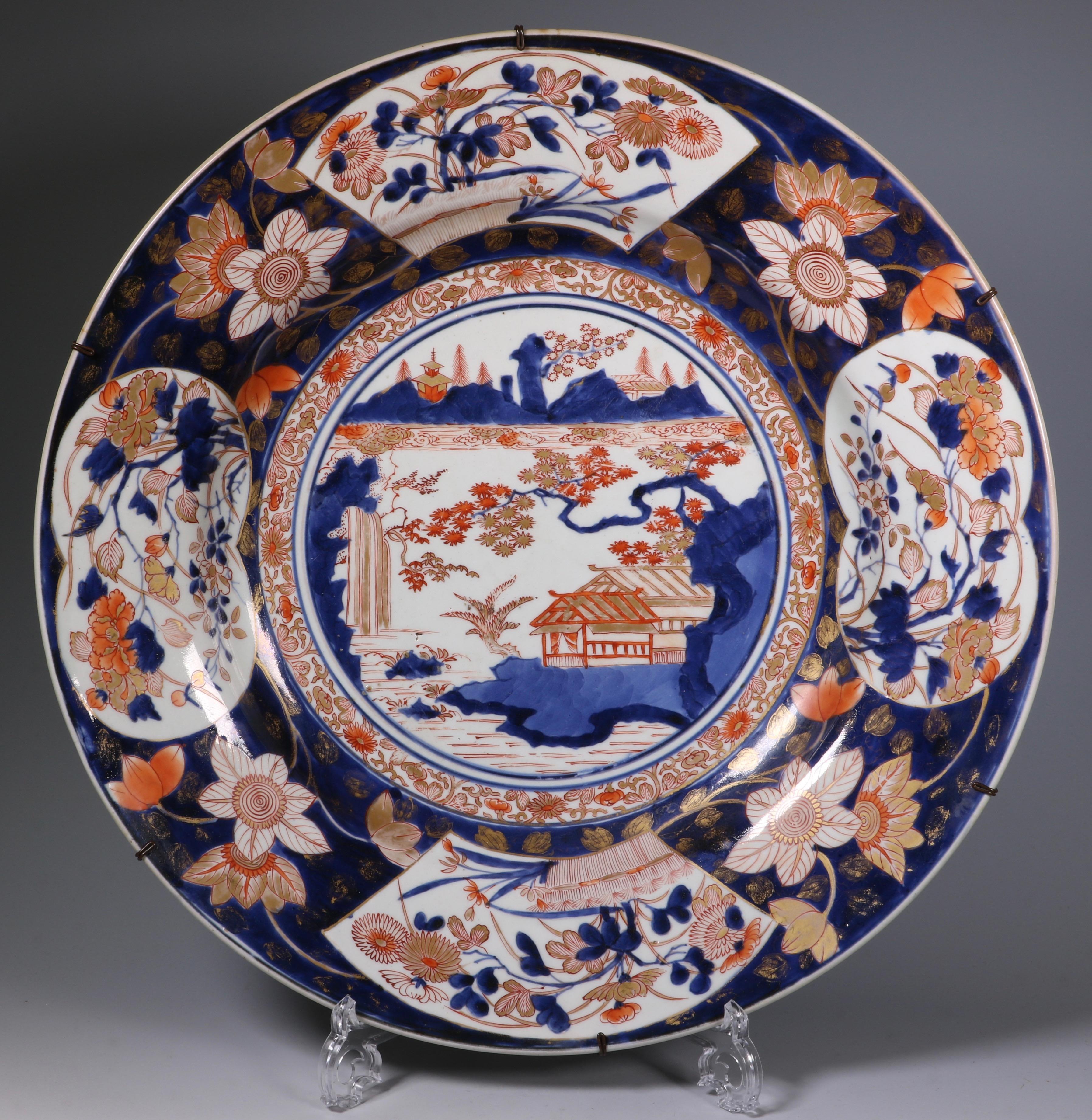 A pair of Imari chargers. Decorated in iron red, gilt and underglaze blue with a central lakeside scene, the rim with various flowers on a dark blue ground. The reverse with a continuous peony scroll.

