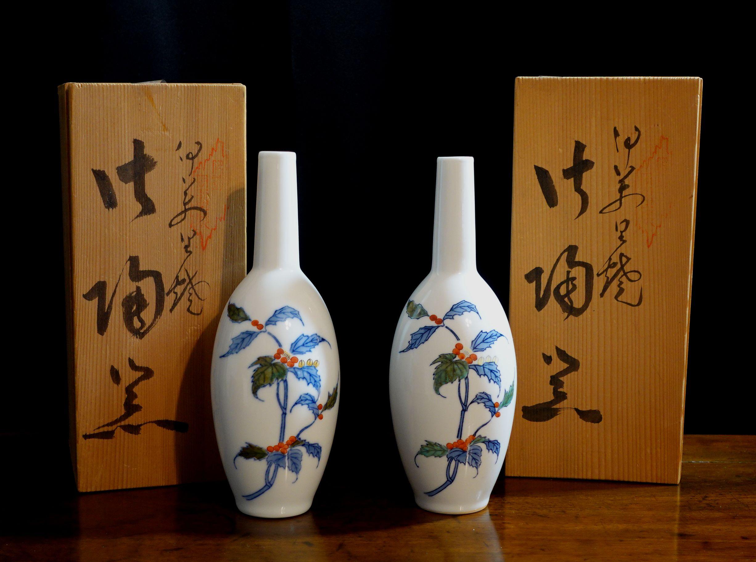 These are two high-quality porcelain sake bottles made in Japan from the Mid 20th century and with the original boxes and paperwork. The artist also signed and stamped on the boxes. Both have the mark on the bottoms indicating the place in Japan