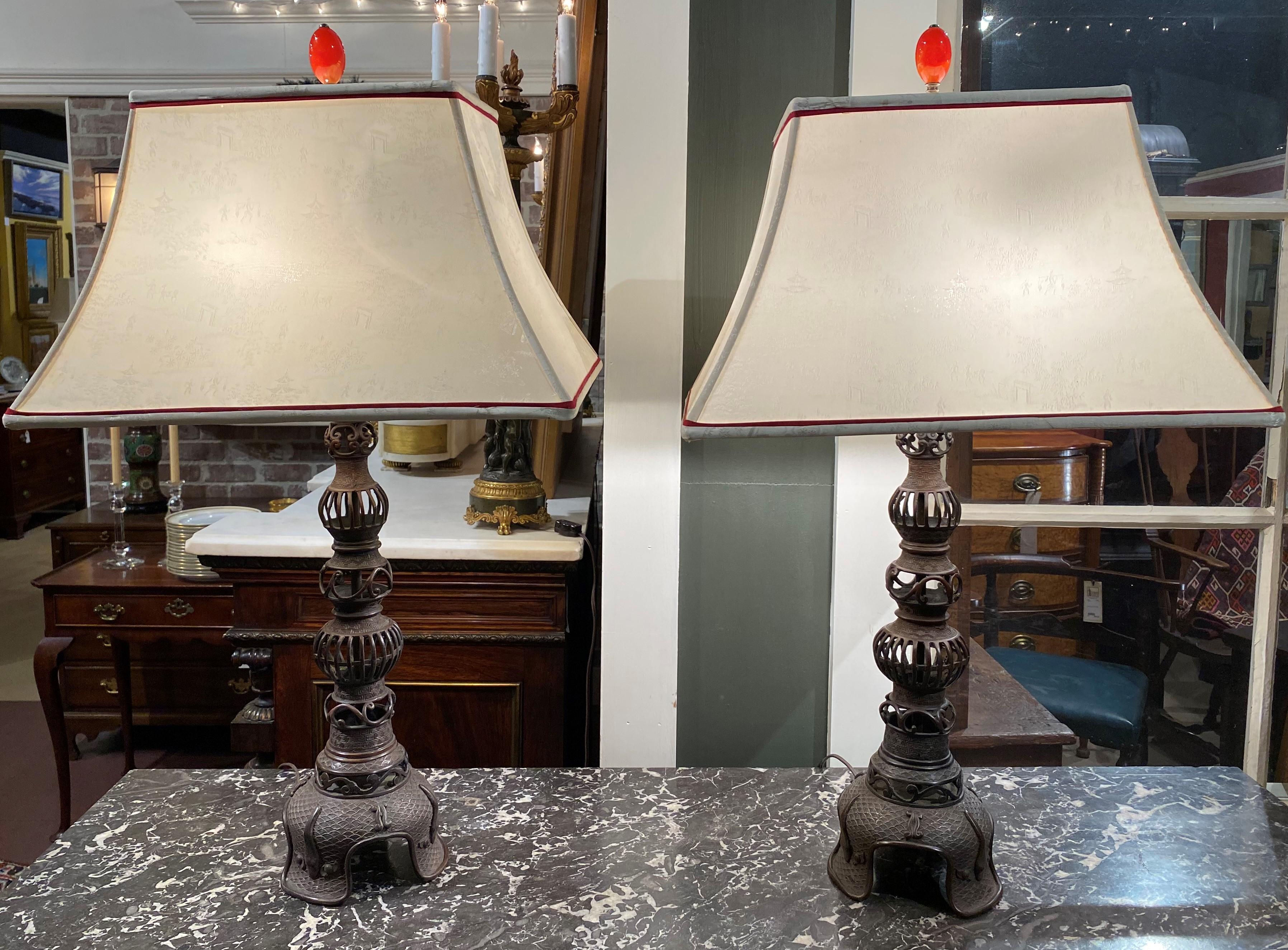 A fine pair of Japanese Meiji two-light reticulated bronze table lamps with bulbous stems, footed bases, silk rectangular shades with pagodas, figures and landscapes, accented with a pair of red stone drop finials. The pair probably date to the turn