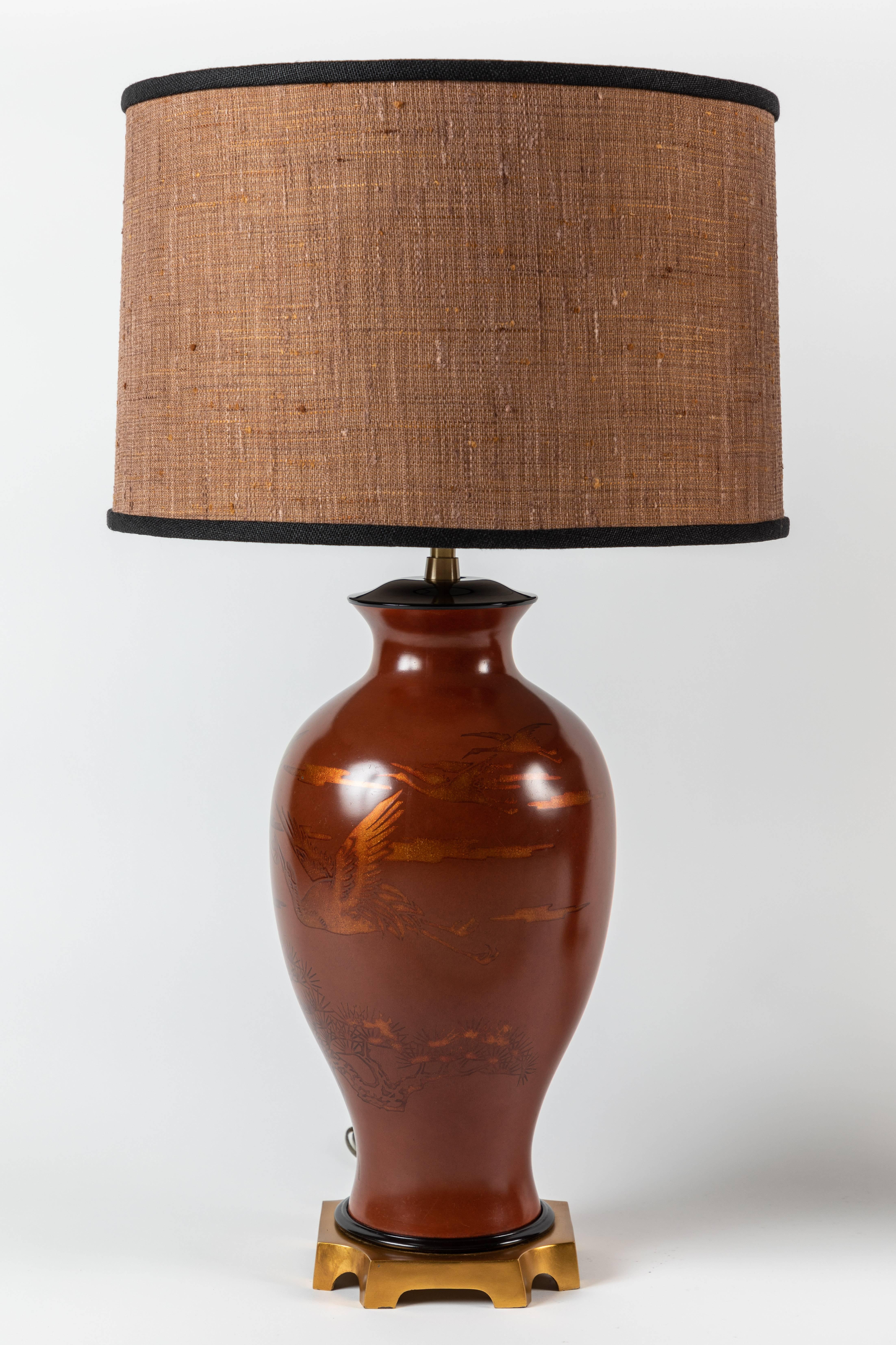 An exquisite pair of red ochre urn-shaped table lamps depicting flying storks / cranes and Japanese scenery. The urns are situated on a gilded rectangular platform. The urns are a sturdy paper mâché material.

Offered with newly-designed custom