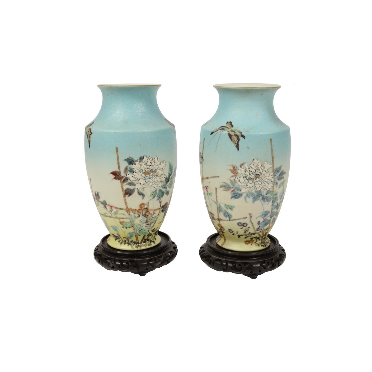 Paire de vases en porcelaine polychrome représentant des fleurs et des papillons décorés à la main, avec base en bois sculpté. Fabrication japonaise, début des années 1900, signée sur la base. 
Bon état. Dimensions : Hauteur 24,6 cm, diamètre de la