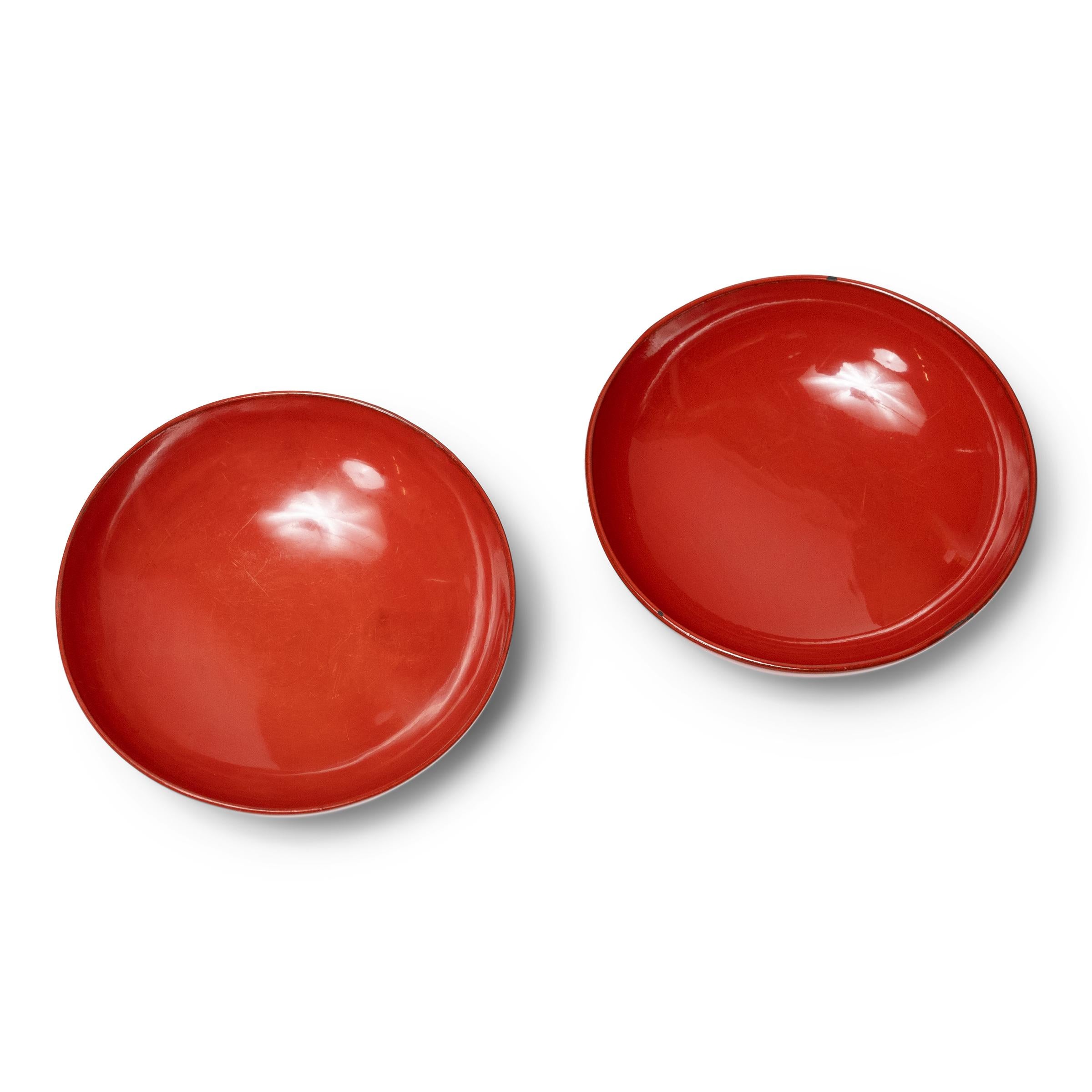 Lightweight and compact, this pair of small footed bowls or bowl lids exemplify the classic Japanese lacquer dishware used daily for food and drink. A glossy red lacquer finish coats each bowl inside and out and highlights its elegantly simple