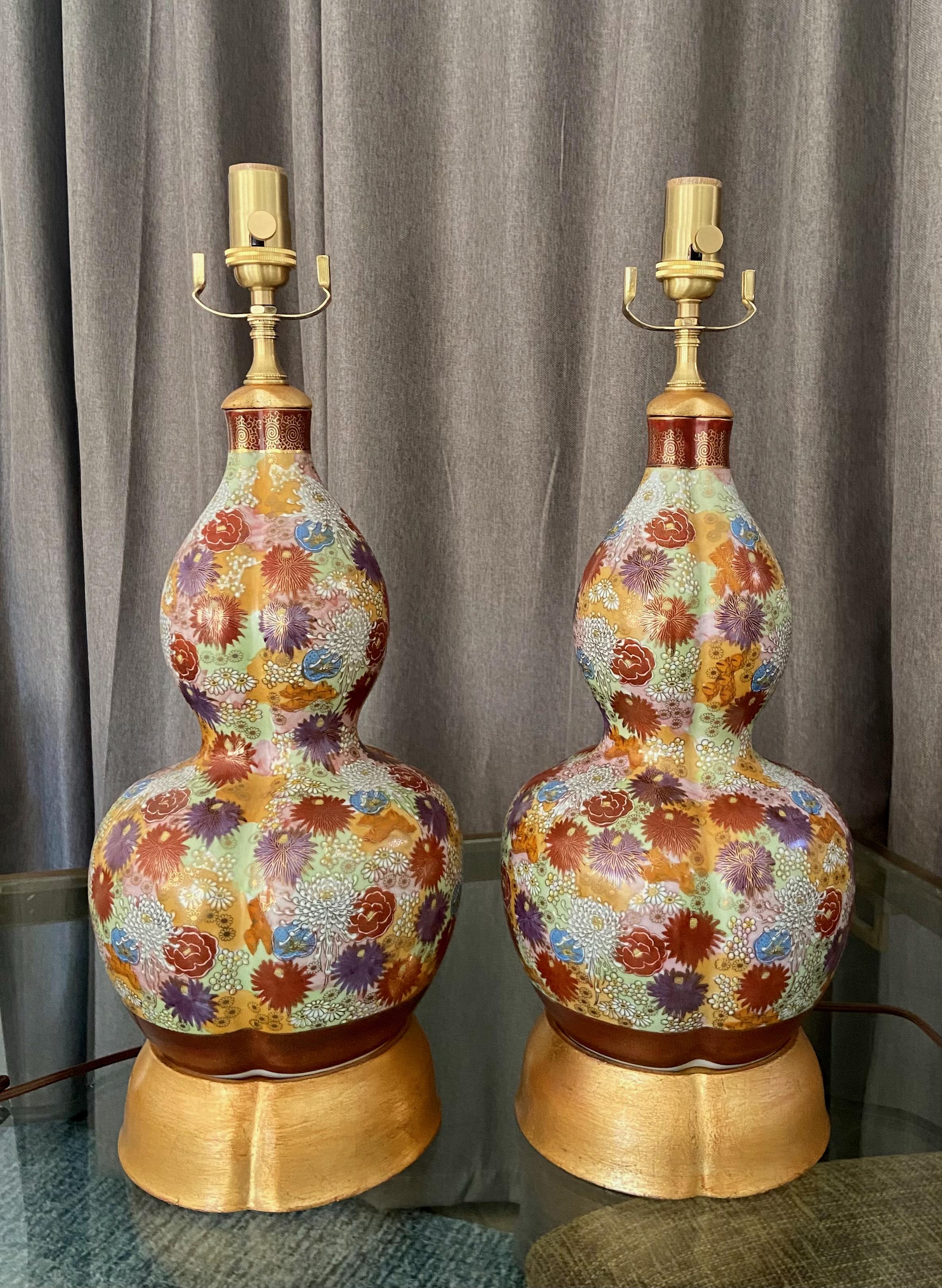 Pair of hand painted floral motif Japanese Satsuma vases mounted on custom gilt turned wood lamp bases. The vases are profusely and expertly painted with different blooms and blossoms in an array of rich colours. Both vases are signed to bottom.
